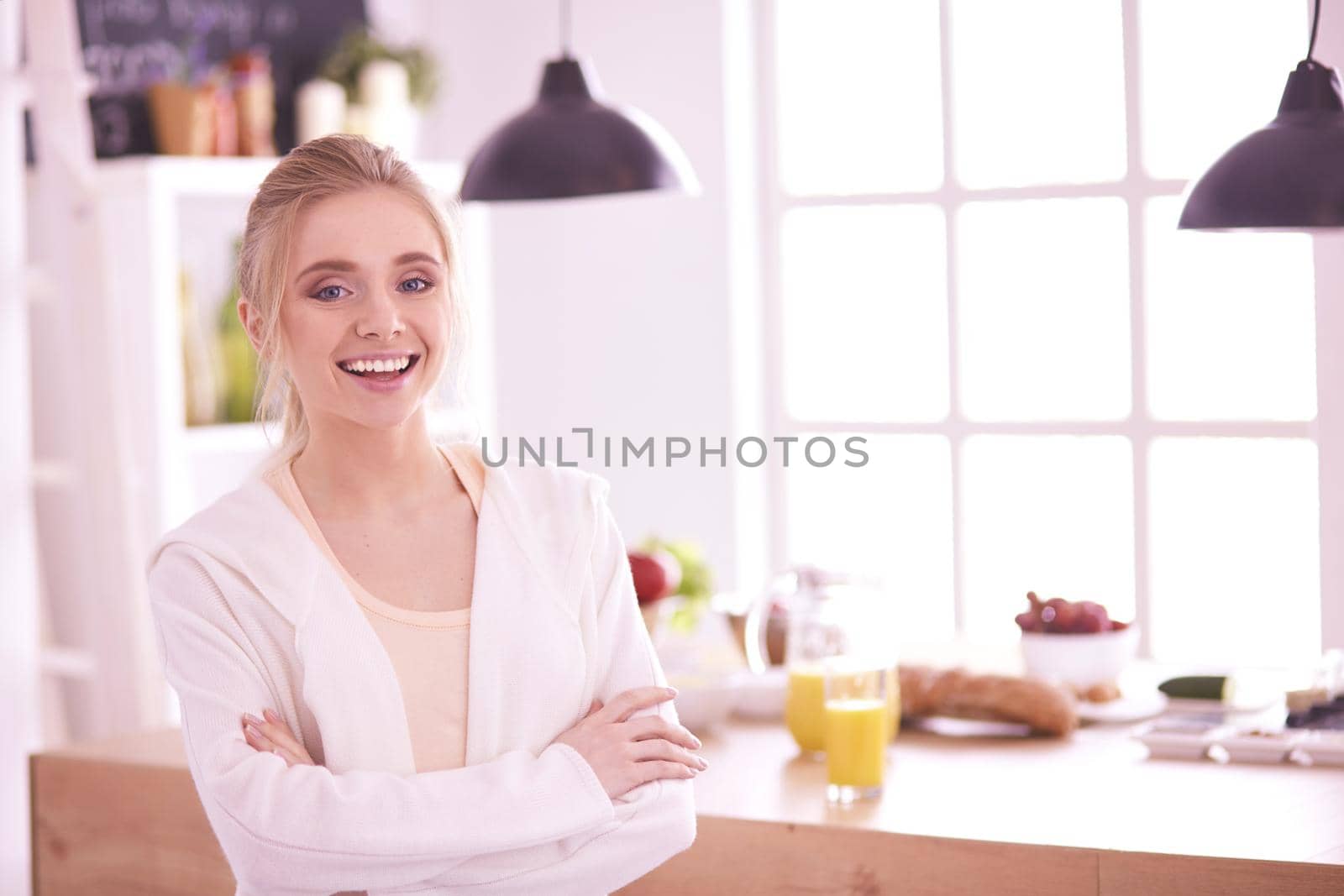 Attractive woman holding a glass of orange juice while standing in the kitchen.