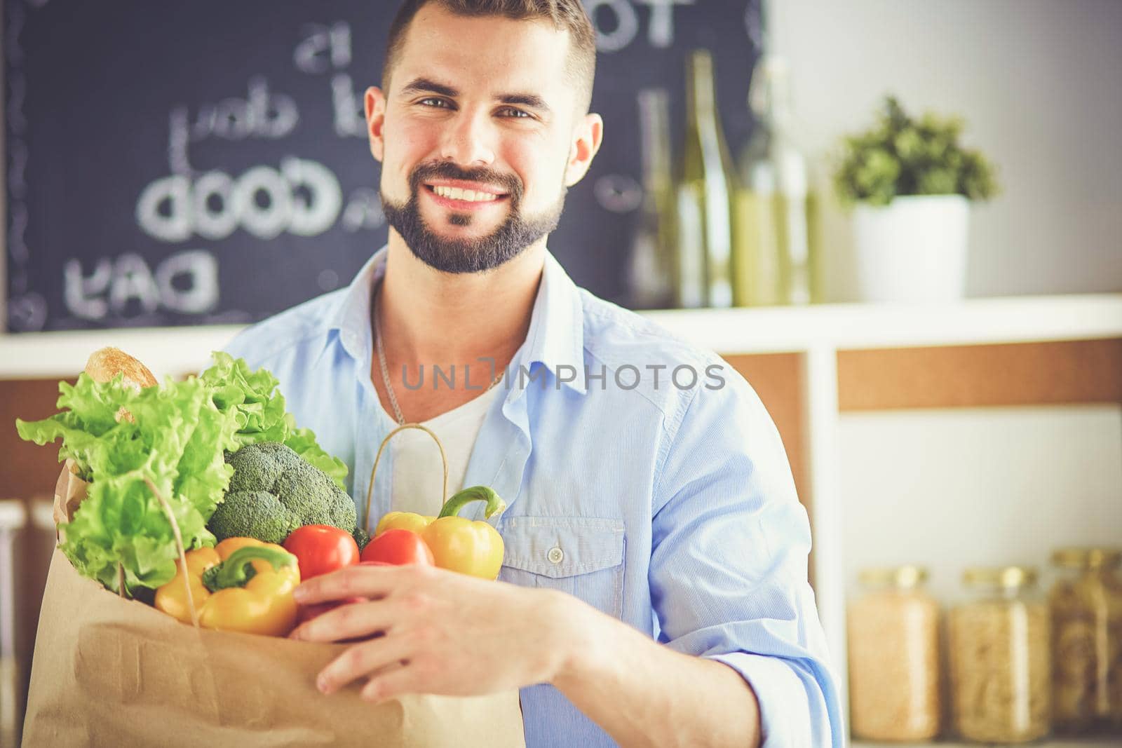 Man holding paper bag full of groceries on the kitchen background. Shopping and healthy food concept.