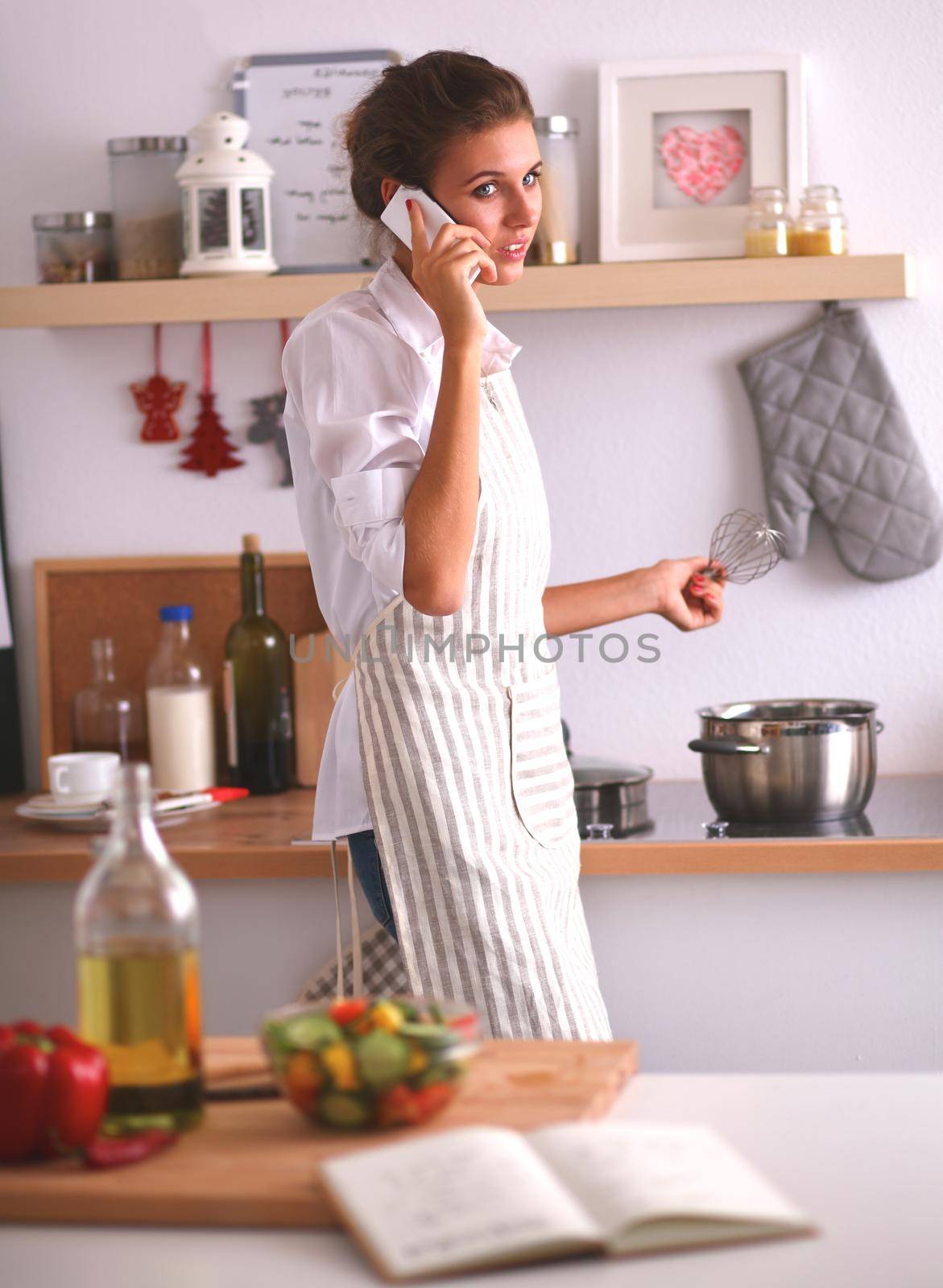 Portrait of a woman with phone in front of vegetables in the kitchen at home