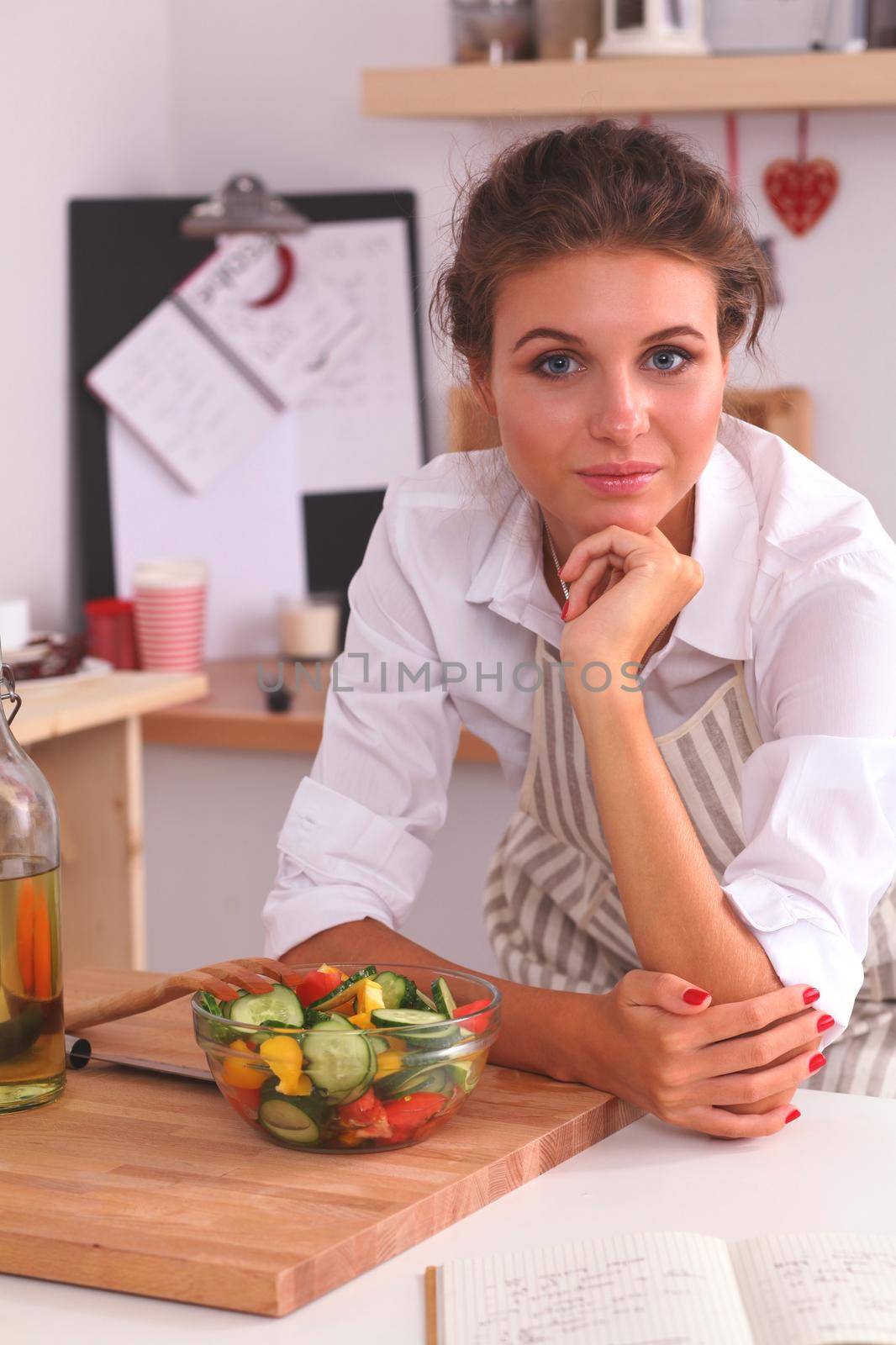 Young woman eating fresh salad in modern kitchen, isolated