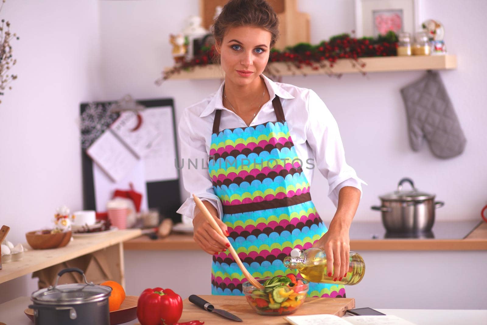 Young woman mixing fresh salad standing near desk .