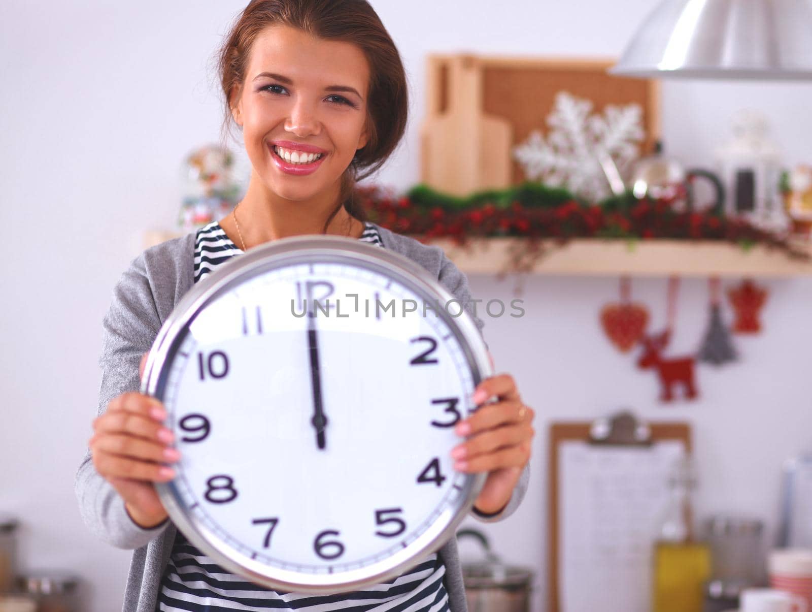 Young woman showing clock in christmas decorated kitchen
