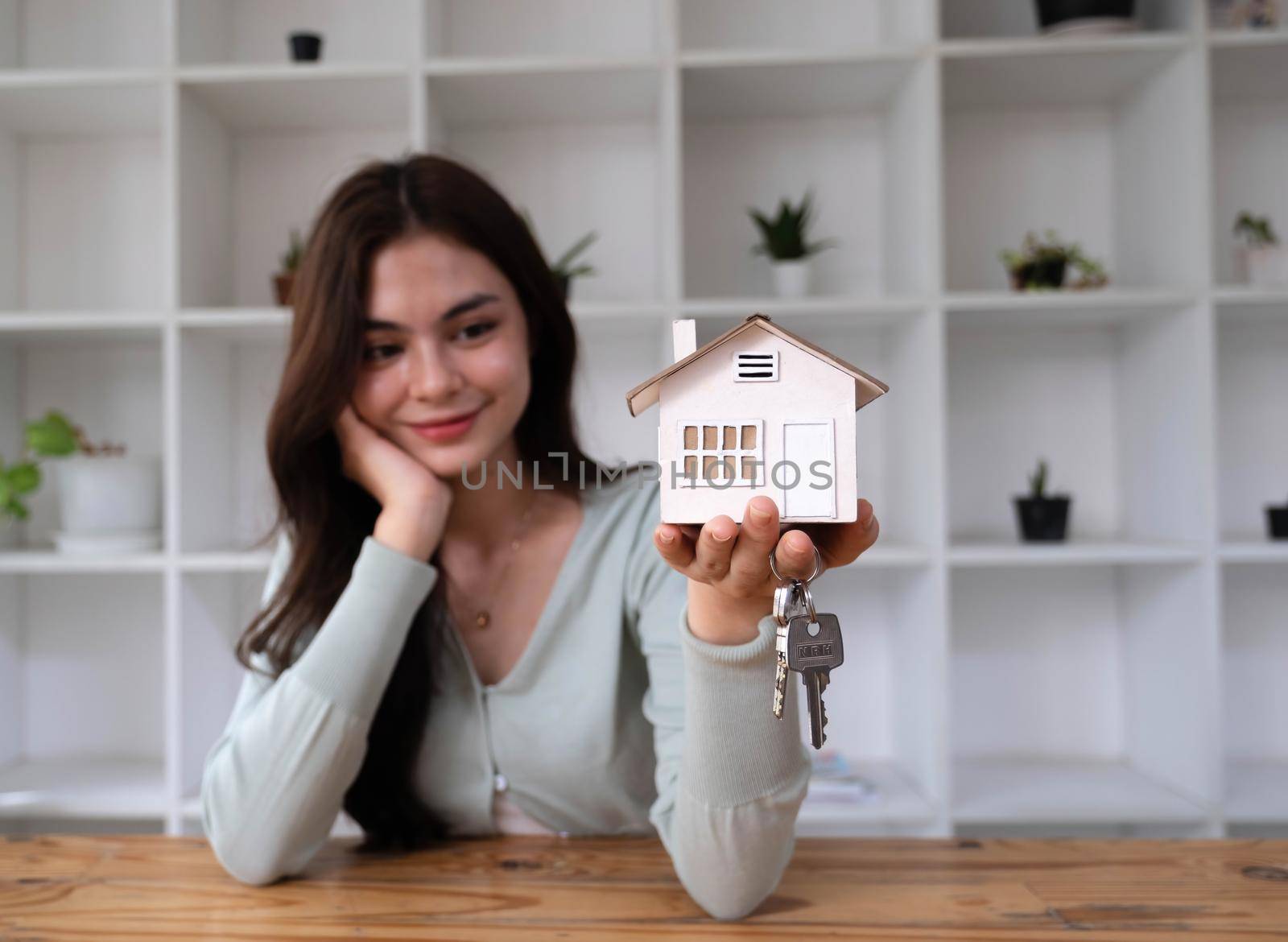 Small house model on white table with real estate agent holding keys in background. Concept of Investment property..