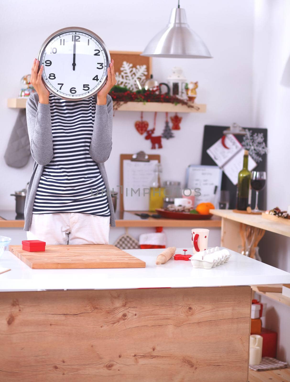 Young woman showing clock in christmas decorated kitchen