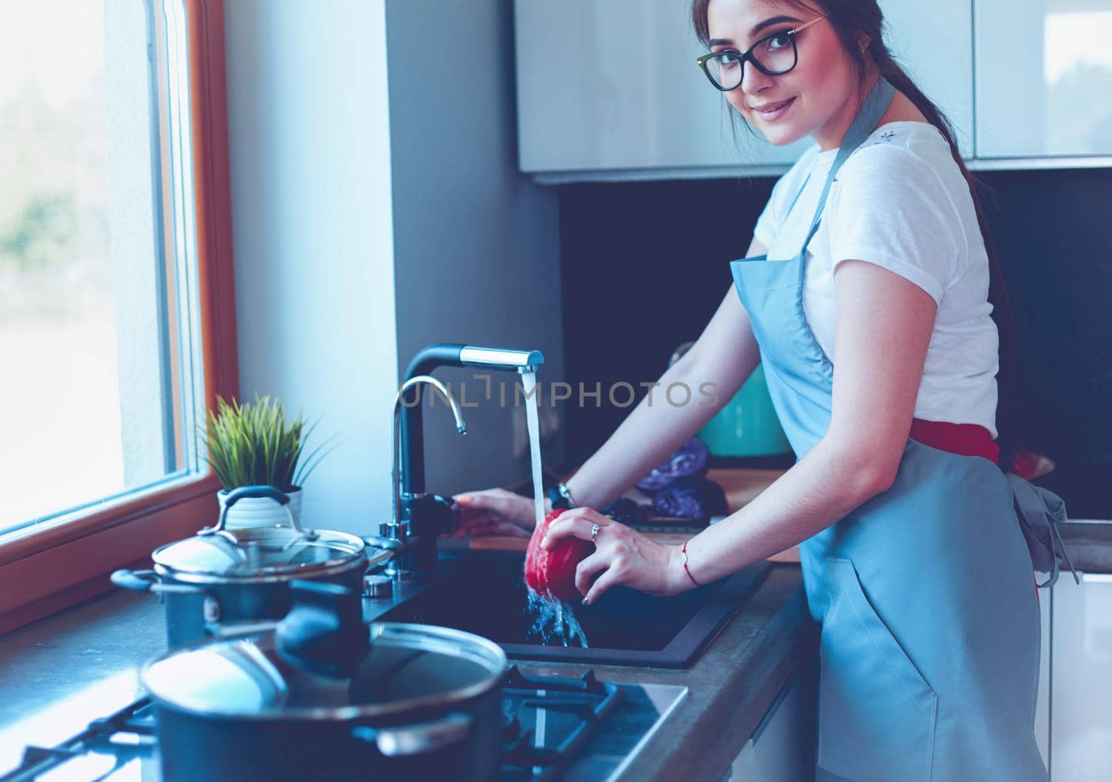 Woman washing vegetables. Beautiful young woman washing vegetables for salad and smiling while standing in the kitchen.