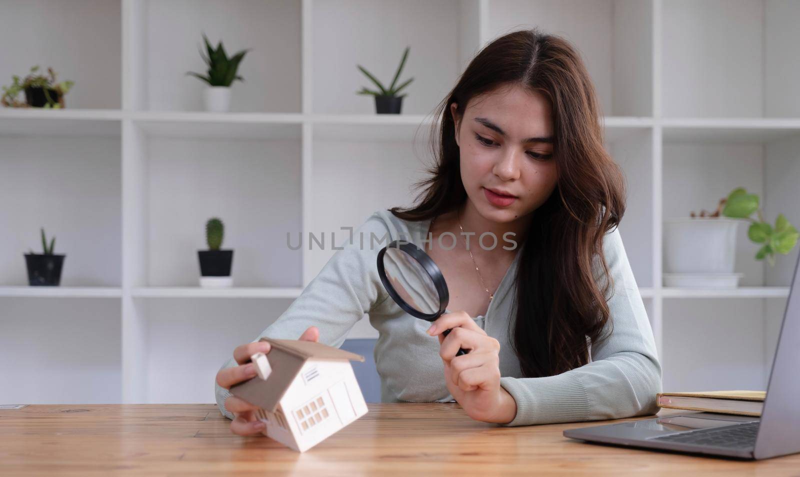Happy woman hand holding magnifying glass and looking at house model, house selection, real estate concept..