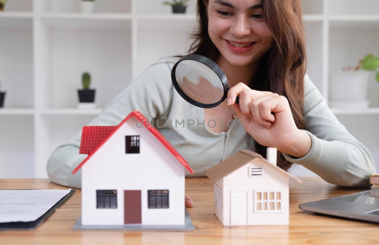 Happy woman hand holding magnifying glass and looking at house model, house selection, real estate concept..