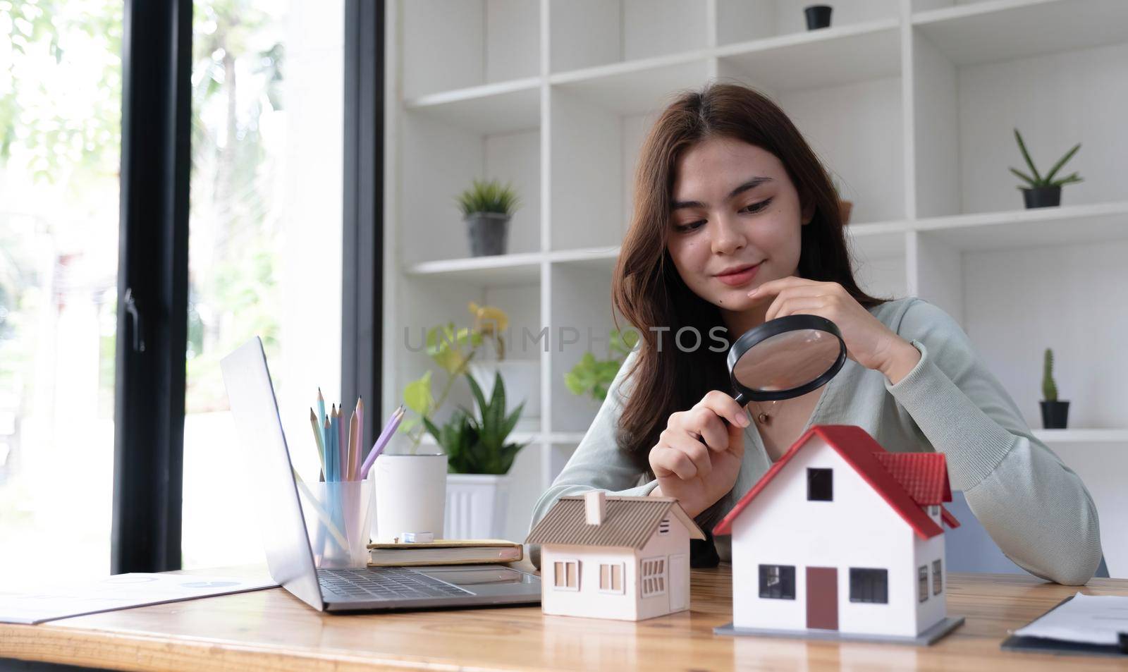 Happy woman hand holding magnifying glass and looking at house model, house selection, real estate concept. by wichayada