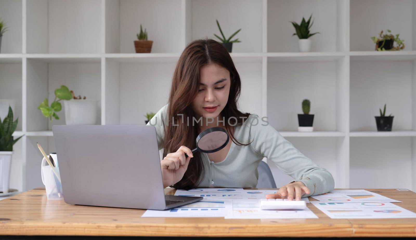 Tax inspector and financial auditor looking through magnifying glass, inspecting company financial papers, documents and reports.