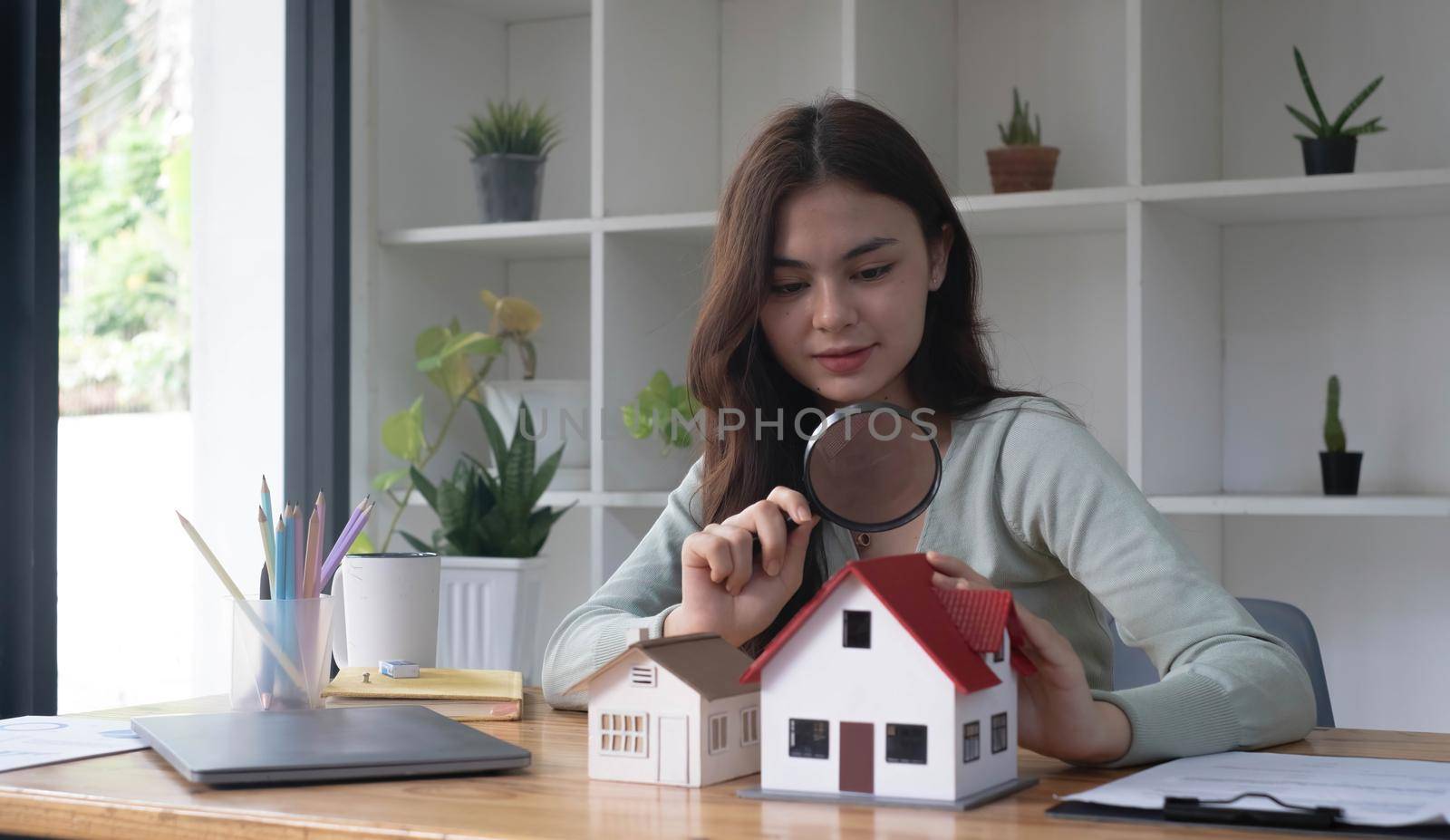 Happy woman hand holding magnifying glass and looking at house model, house selection, real estate concept..