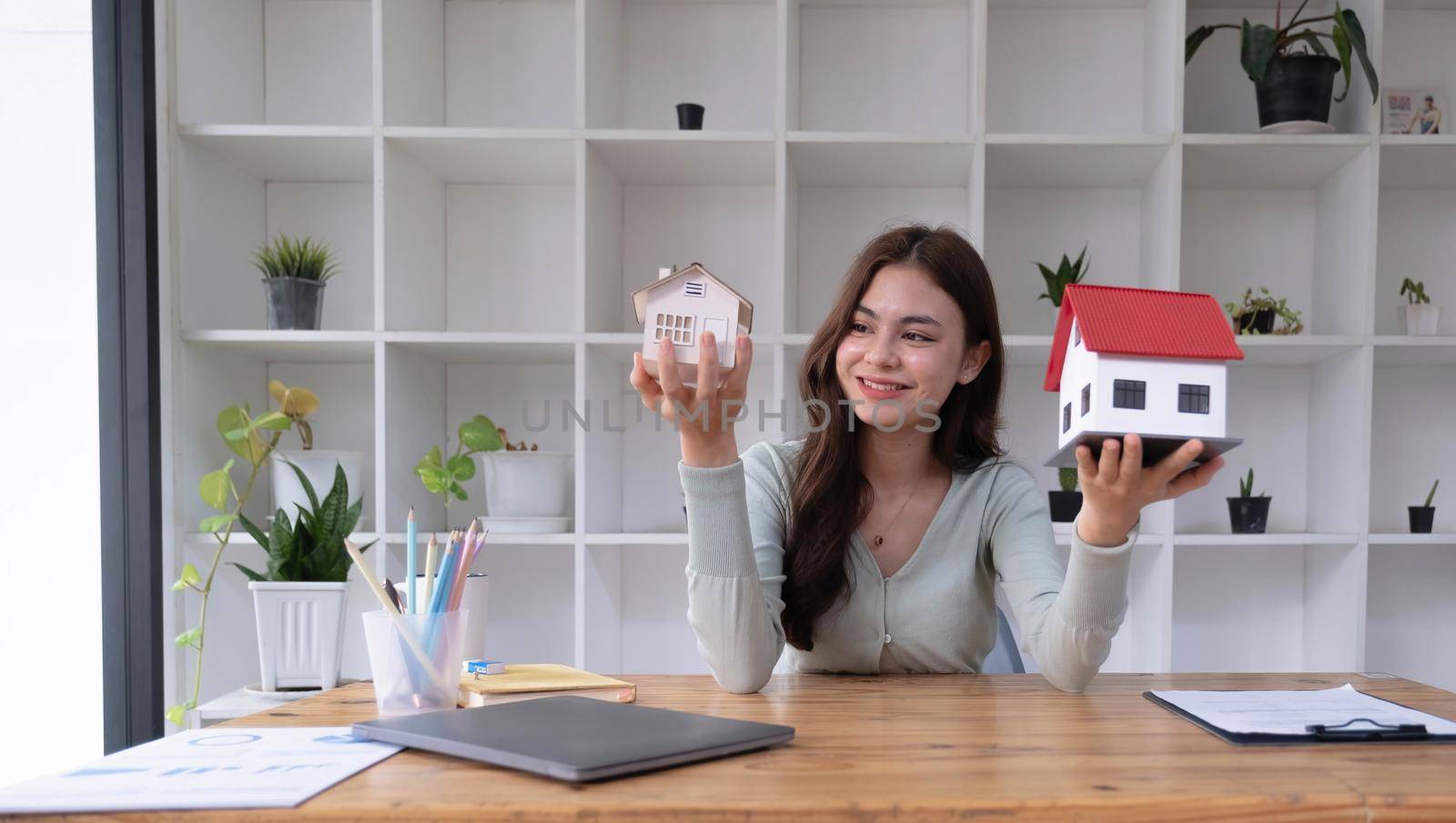 Real estate agent sitting and holding two house model in the office. by wichayada
