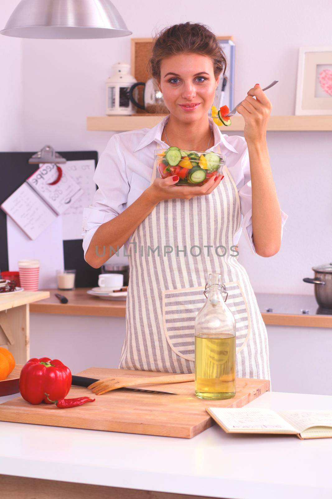 Young woman eating fresh salad in modern kitchen .