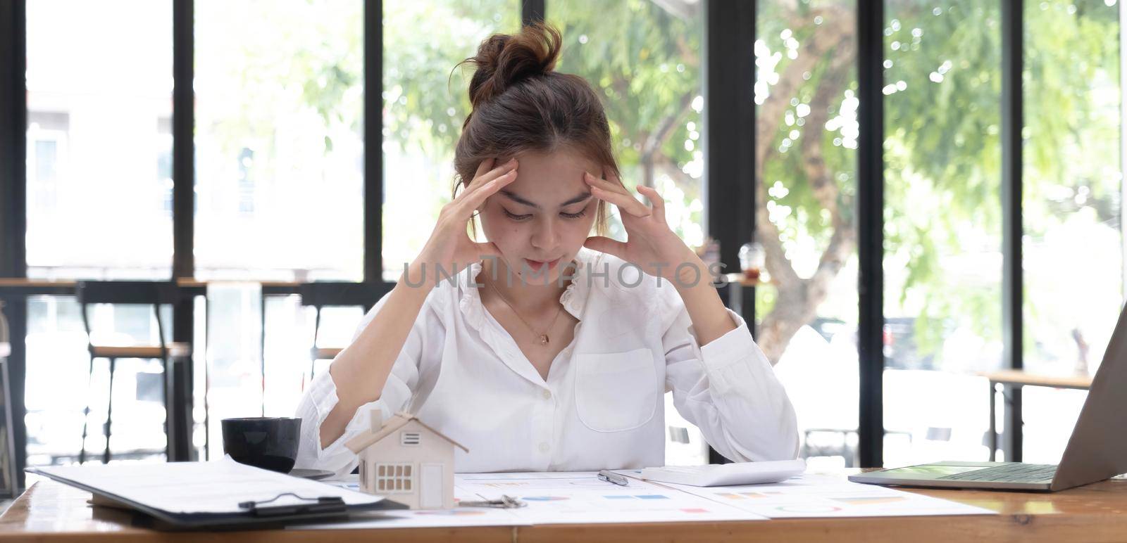 Photo of a tired woman keeps a hand on her head at the wooden working desk after finishing work hard. by wichayada