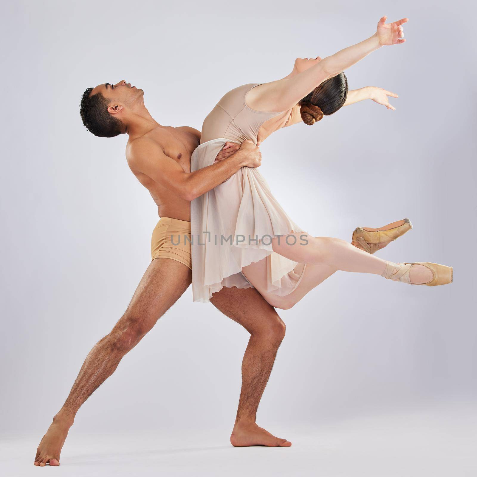 The heart just wants to dance. Studio shot of a young man and woman performing a ballet recital against a grey background. by YuriArcurs