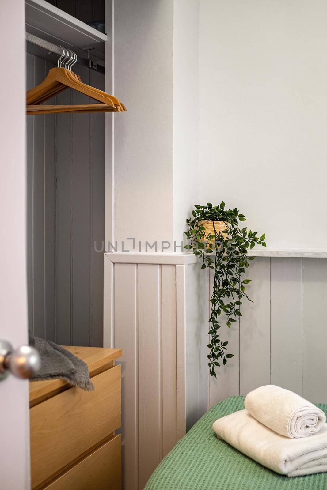 A corner of bedroom with part of bed with towels, green plant and openstyle wardrobe with hangers. by apavlin