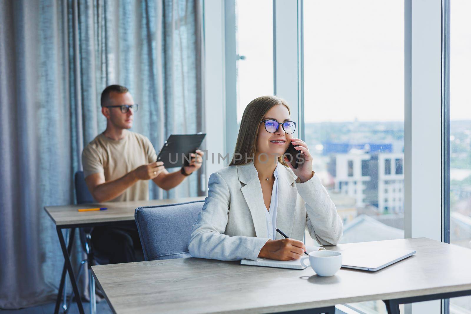 Portrait of a female manager in formal attire doing office work and talking on the phone, a successful european female boss in optical glasses for vision correction, posing at her desk by Dmitrytph