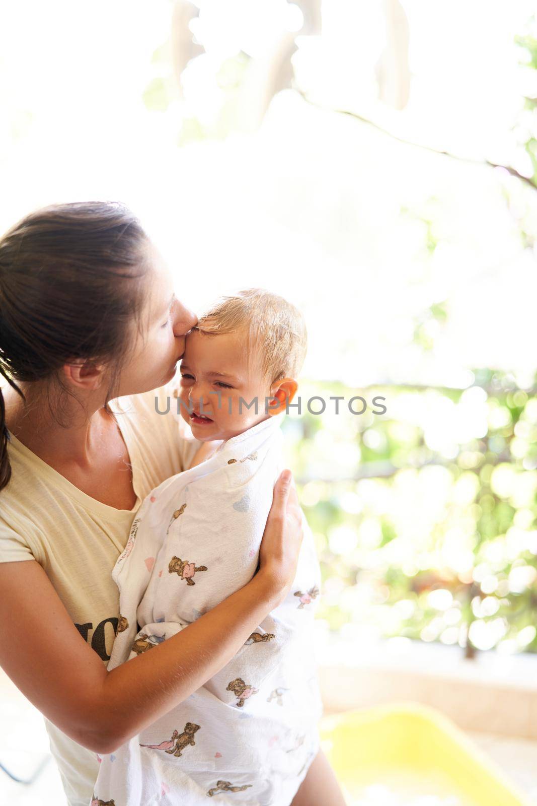 Mom kisses a whimpering baby holding him in her arms by Nadtochiy