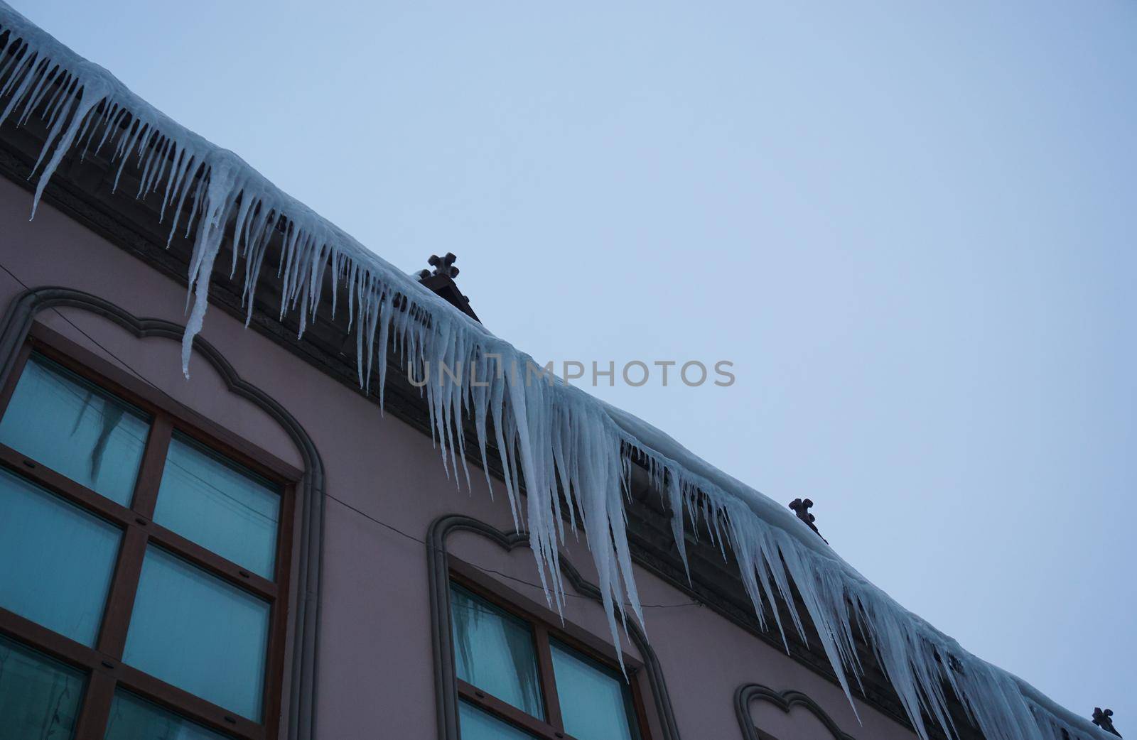 Large icicles of ice hang on the roof of the house by Spirina