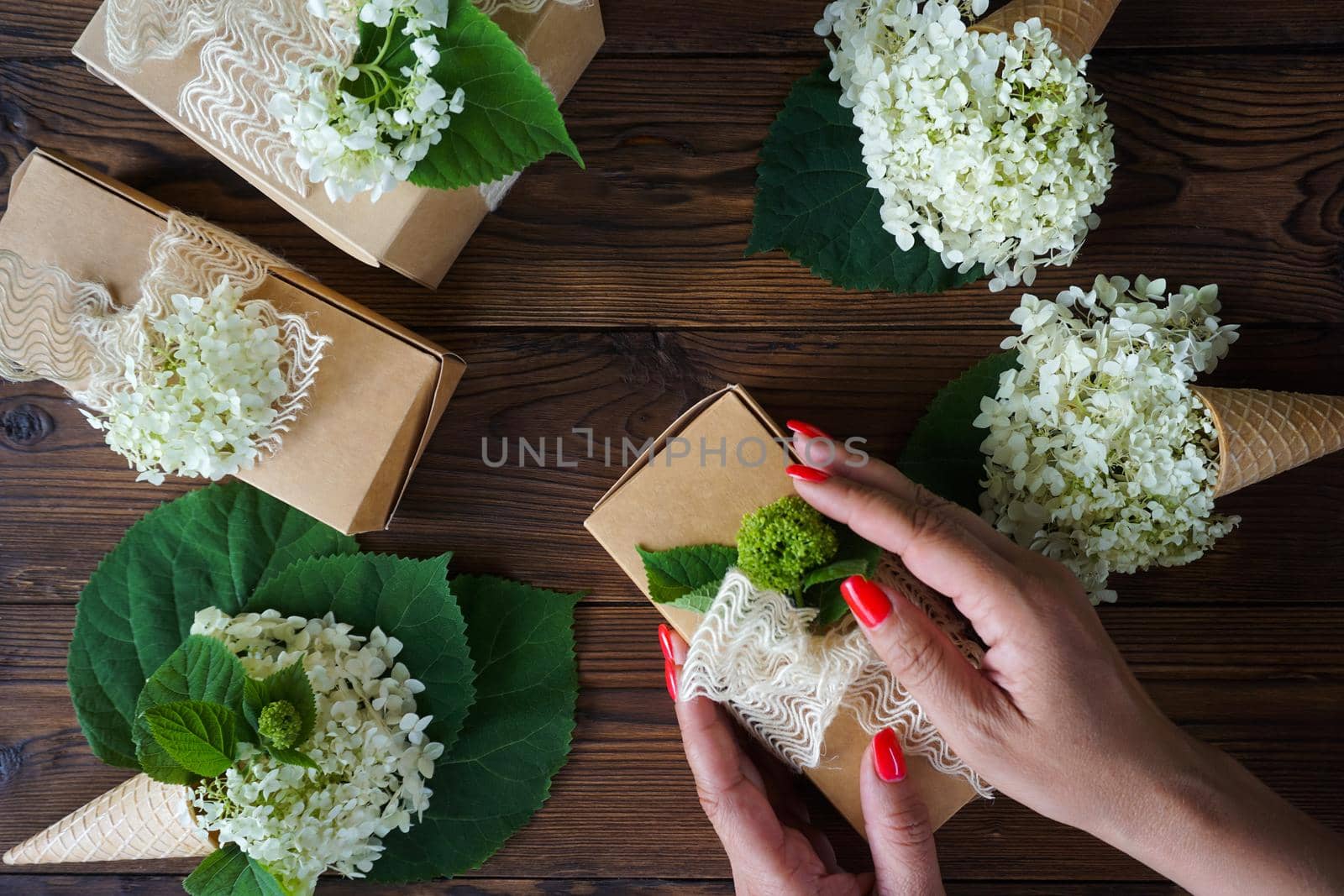 Women's hands pack a gift in a craft box with hydrangea flowers by Spirina