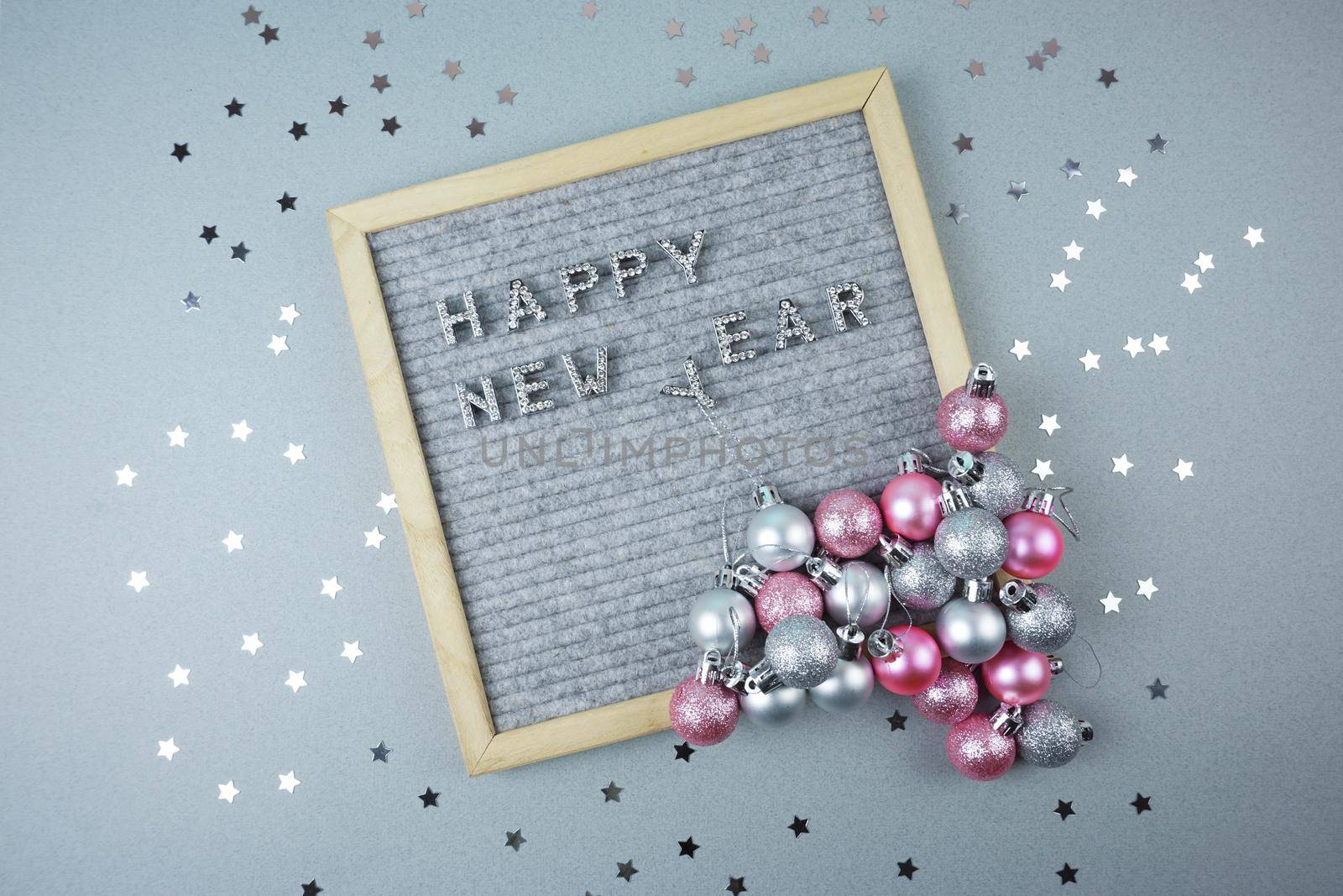 The happy new year inscription is laid out on a gray background decorated with silver stars and Christmas balls by Spirina