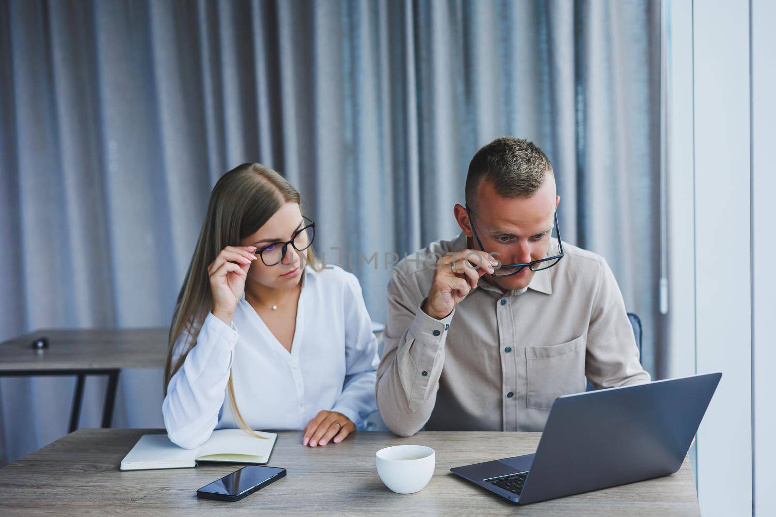 Businessmen are discussing while working with laptop in the office. Focused business people cooperating in a modern workspace. Two young businessmen are sitting together at a table.