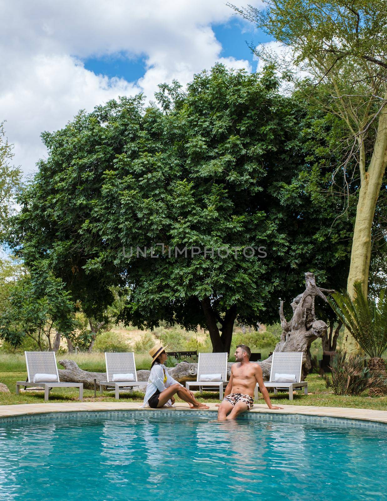 couple men and women on safari in South Africa relaxing by the pool of a luxury safari lodge , by fokkebok