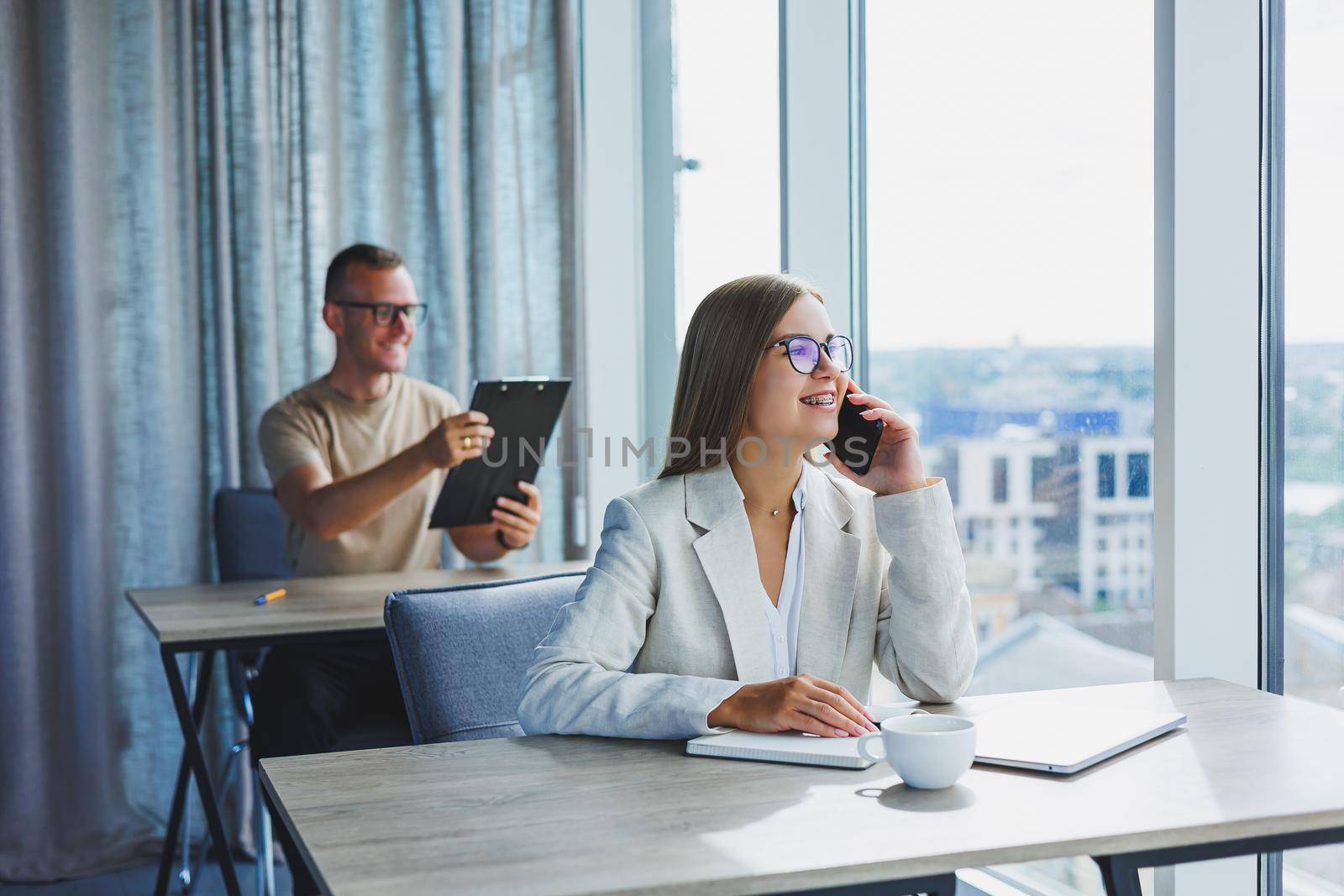 Portrait of a female manager in formal attire doing office work and talking on the phone, a successful european female boss in optical glasses for vision correction, posing at her desk by Dmitrytph