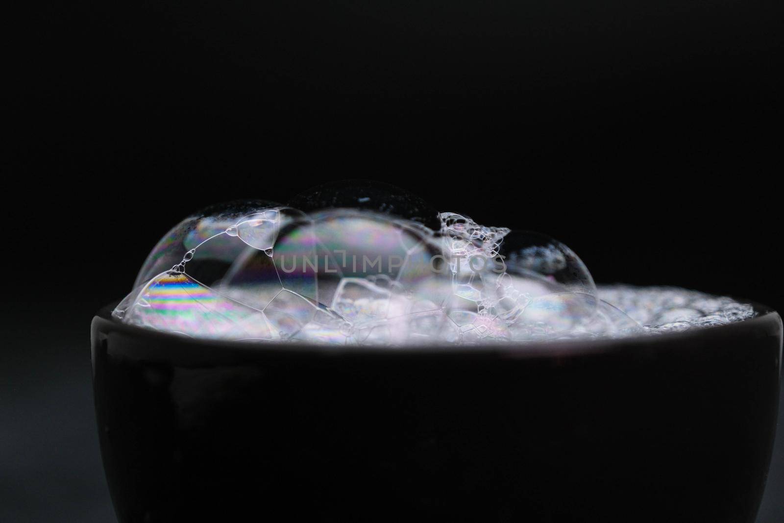 Black cup with foam water and bubbles on black background. Soap bubbles in motion background.