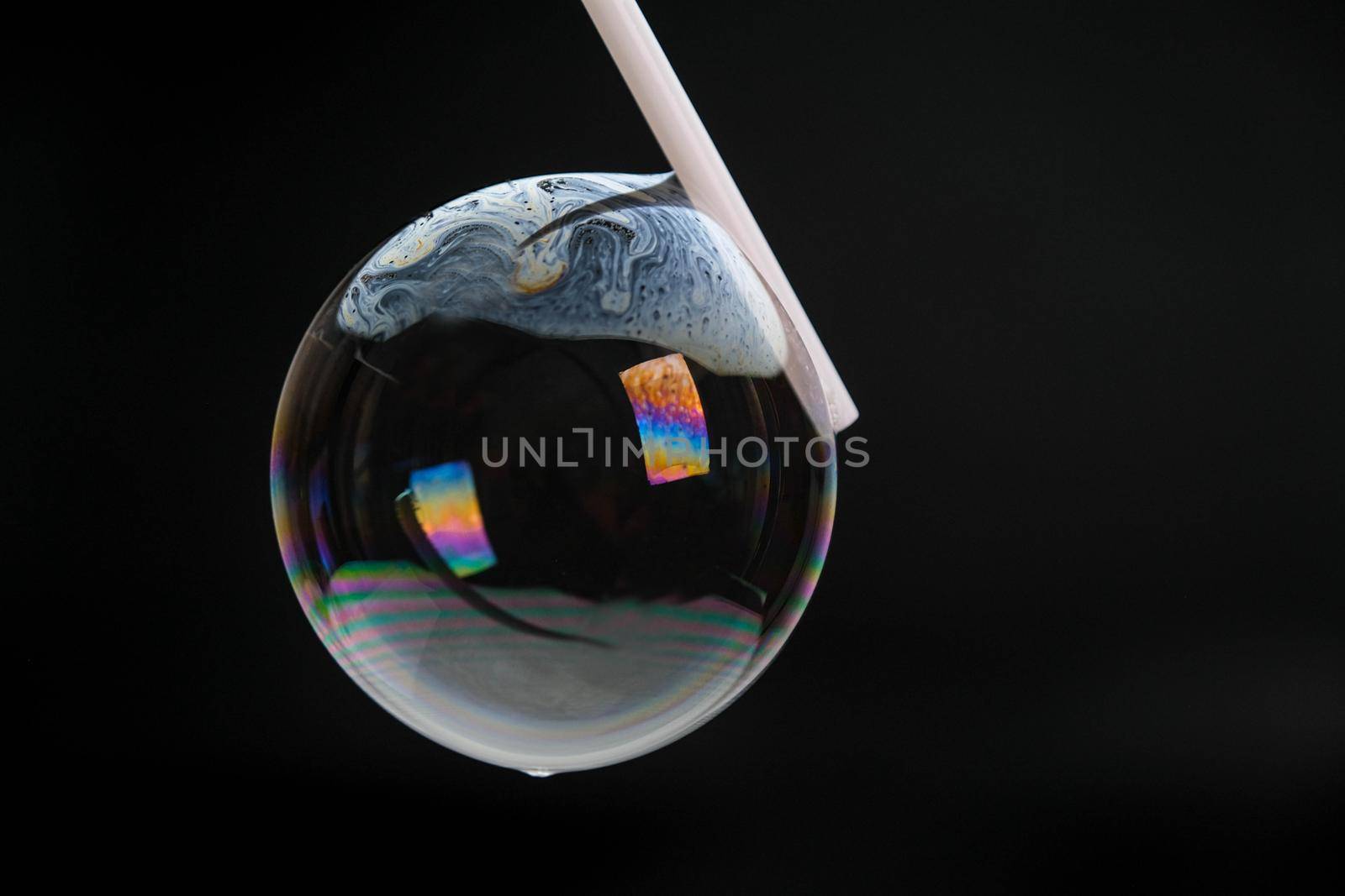 Beautiful soap bubbles are blown with a straw on a black background. Abstract soap bubbles with colorful reflections. by TEERASAK