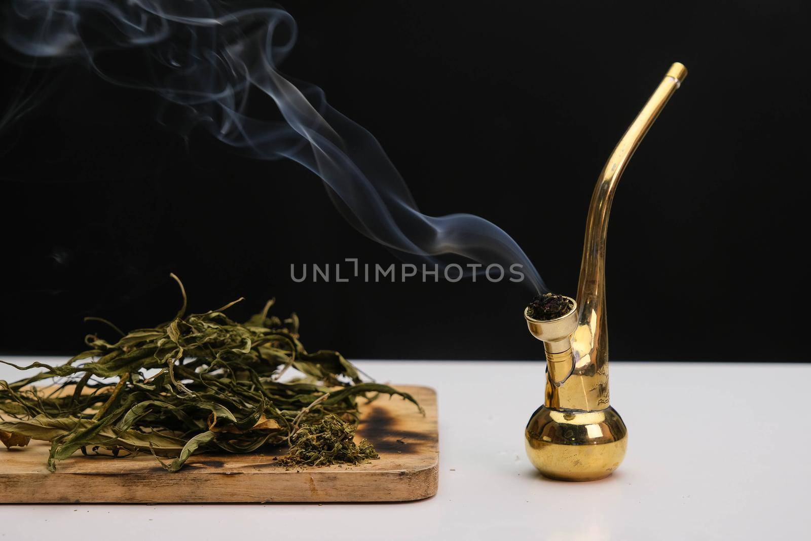 Close-up of cannabis leaves on a wooden board and smoke coming out of a pipe on a black background. Cannabis legalisation.
