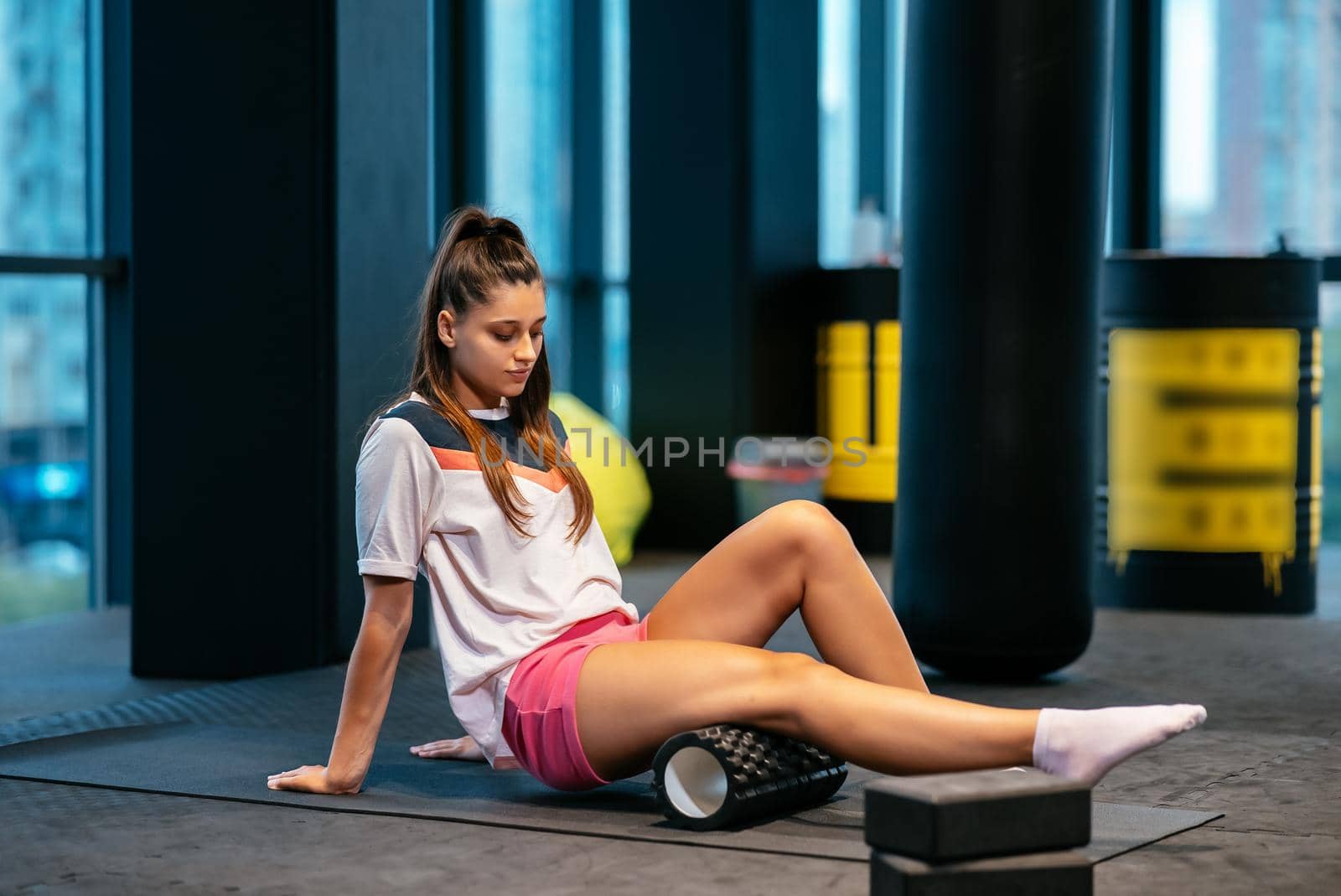 Young woman using a foam roller while doing stretching exercises in the gym.