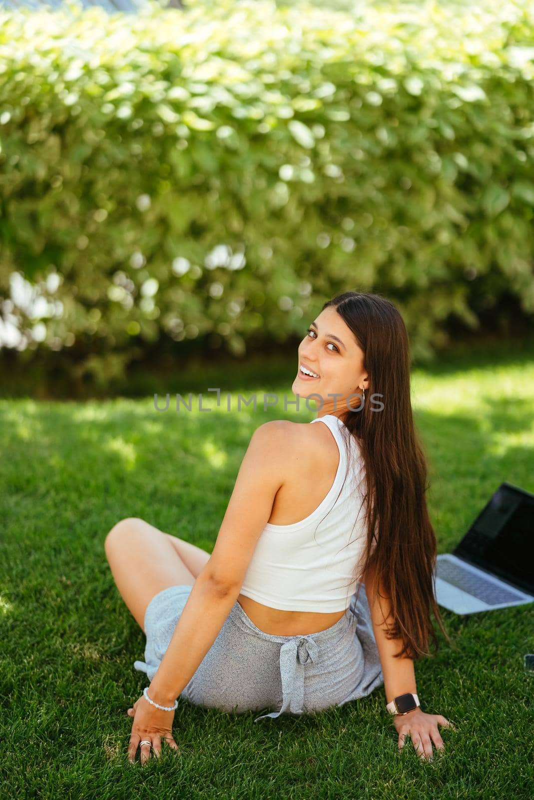 The concept of remote work. A young girl works with a laptop in the fresh air in the park, sitting on the lawn.