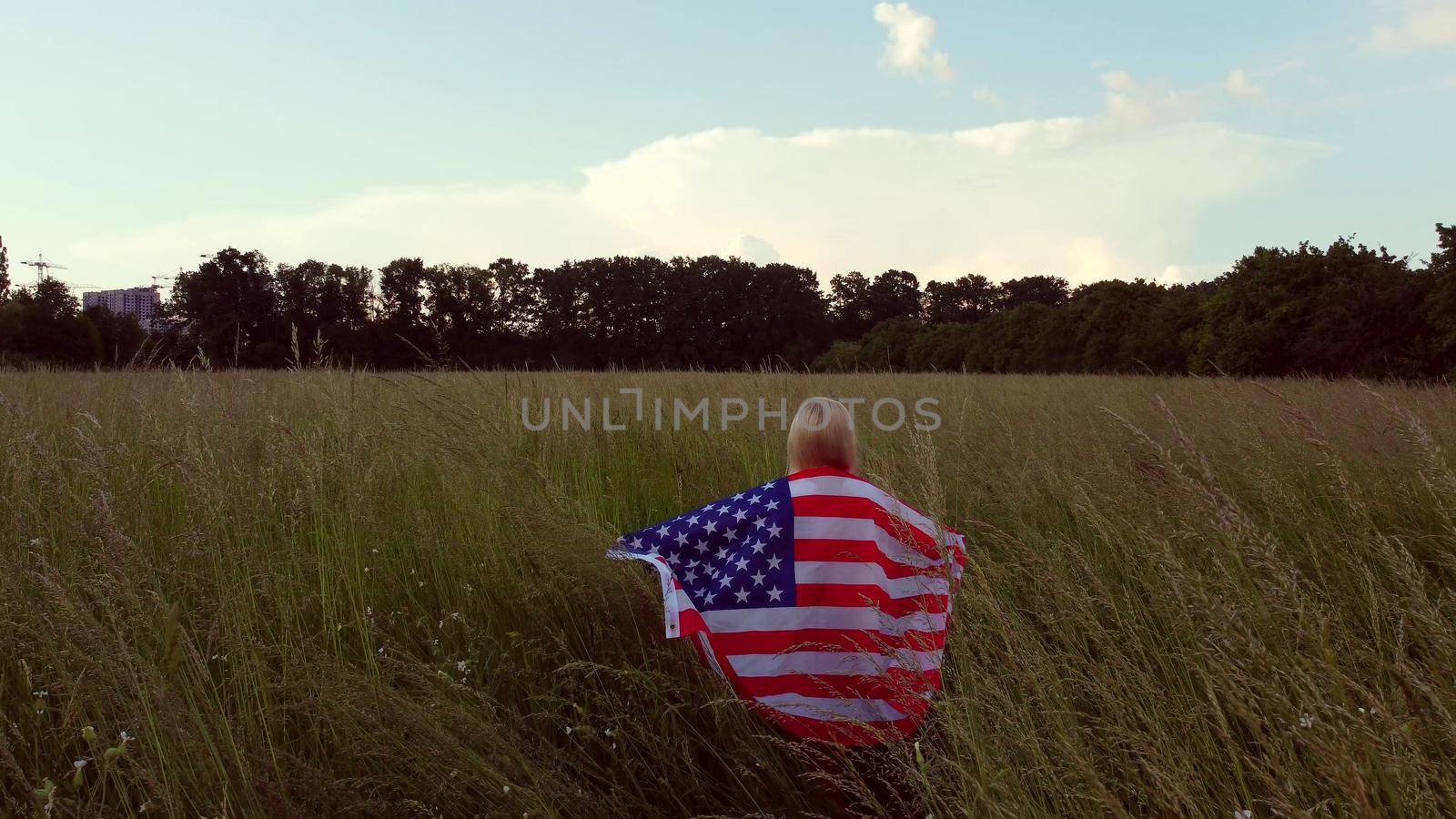 Young happy woman waving USA stars and stripes flag in golden sunset sunshine field by Andelov13