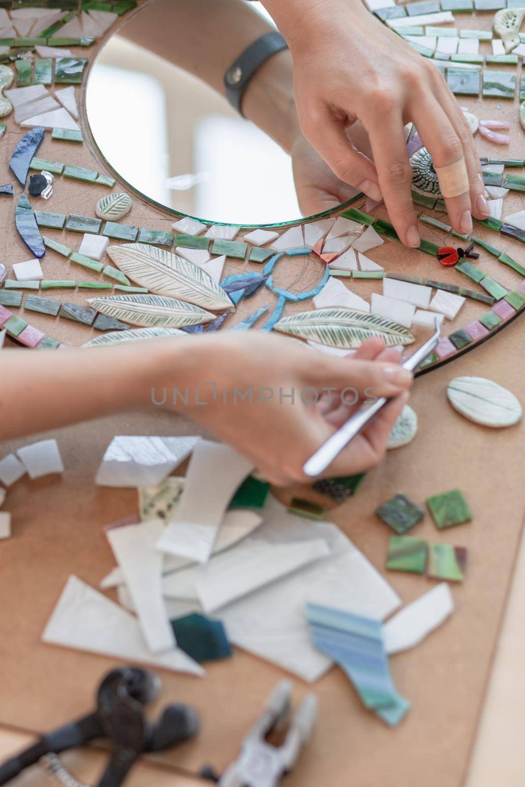 Workplace of the mosaic master: women's hands holding tool for mosaic details in the process of making a mosaic. Close-up. Creative process. Masterclass handmade