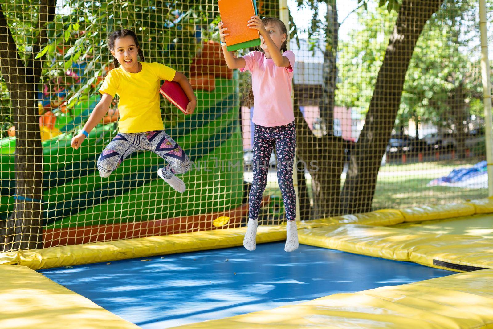 Little pretty girls having fun outdoor. Jumping on trampoline in children zone. Amusement park.