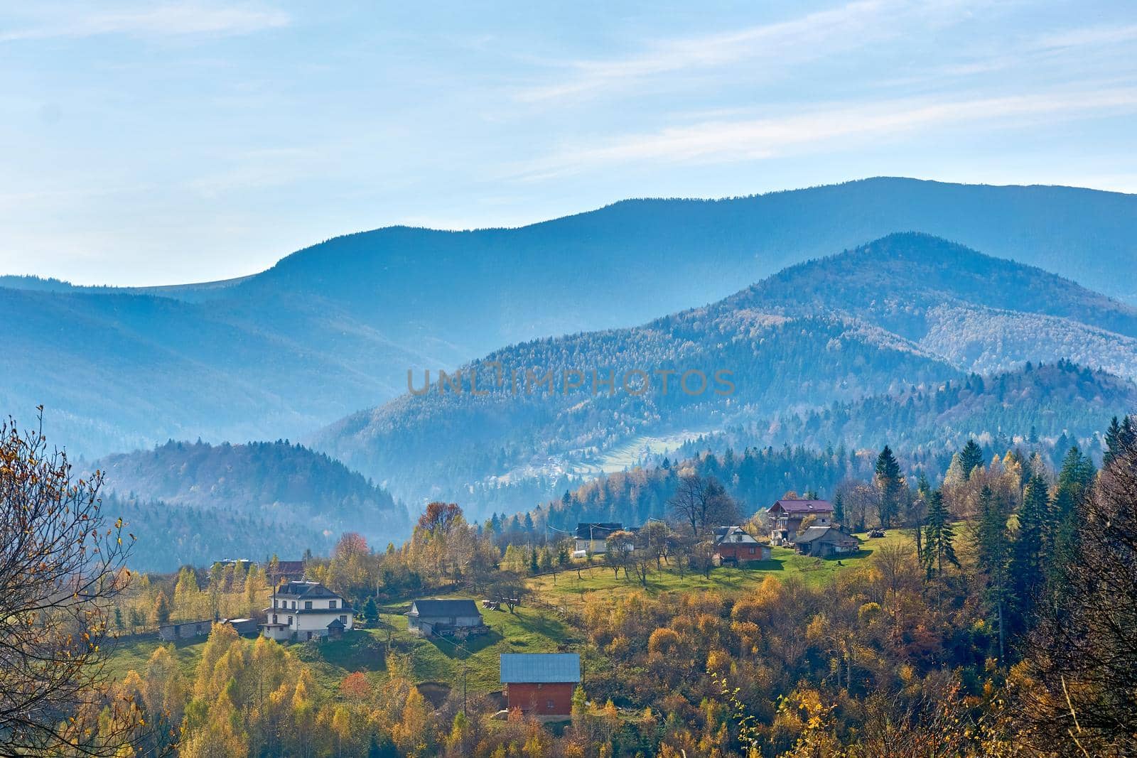 Autumn is one of the four temperate seasons. Outside the tropics, autumn marks the transition from summer to winter. Aerial view of an autumn small village in a valley and mountains in a blue haze