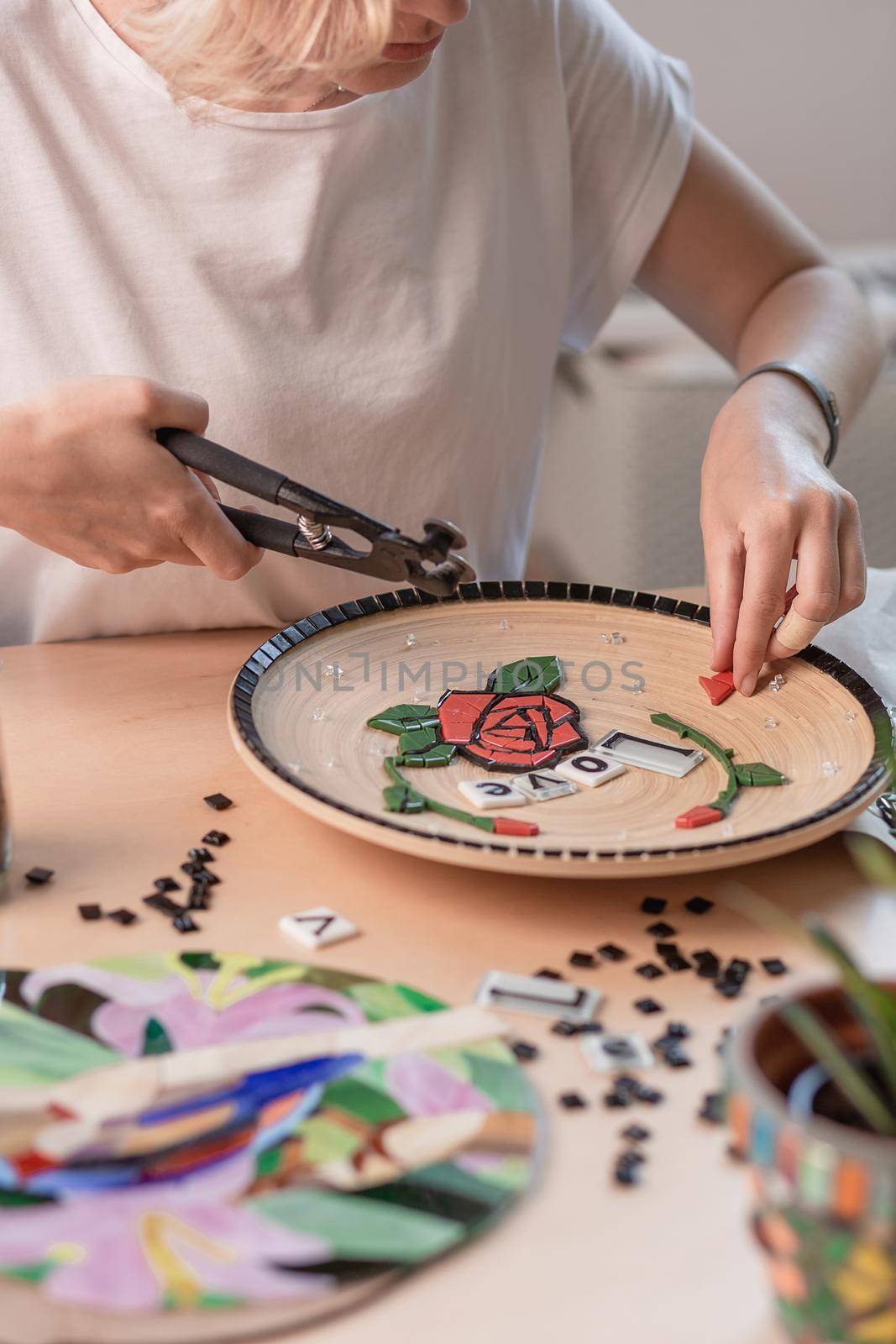 Workplace of a mosaic master: female hands laying out a mosaic element on the table by nazarovsergey