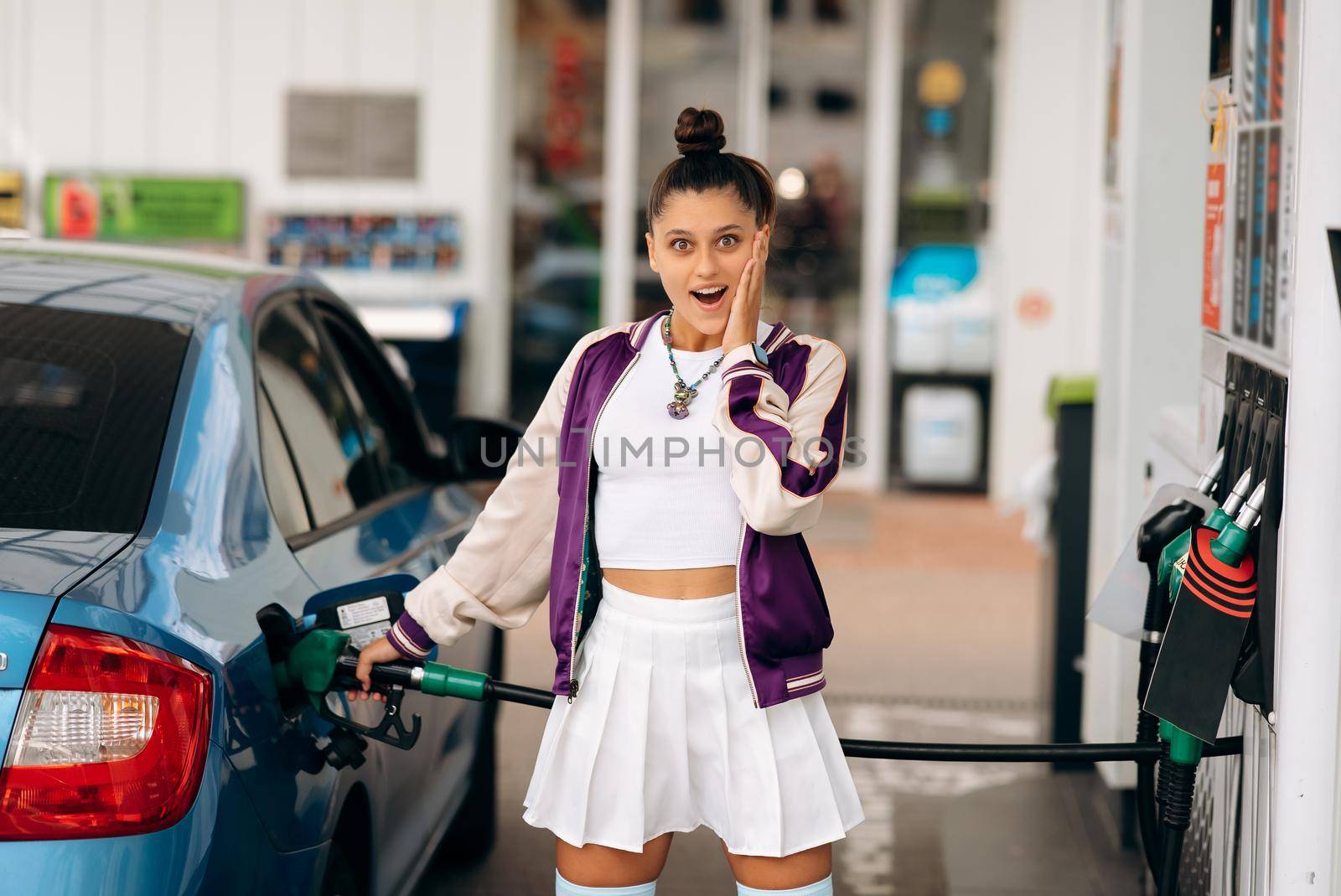 Cheerful young woman brunette filling her car with fuel at a gas station