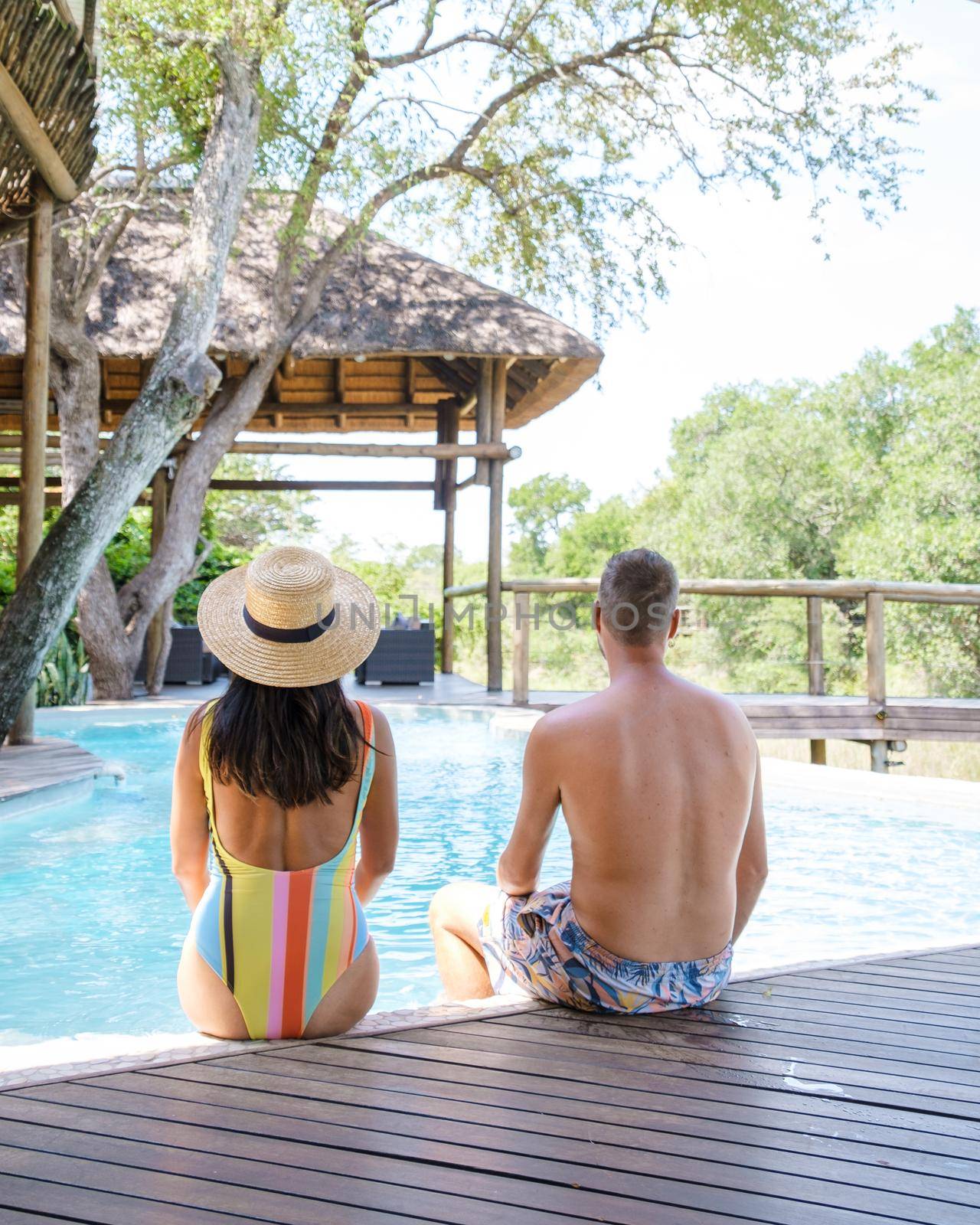 couple men and women on safari in South Africa relaxing by the pool of a luxury safari lodge , Asian women and European men on safari in South Africa