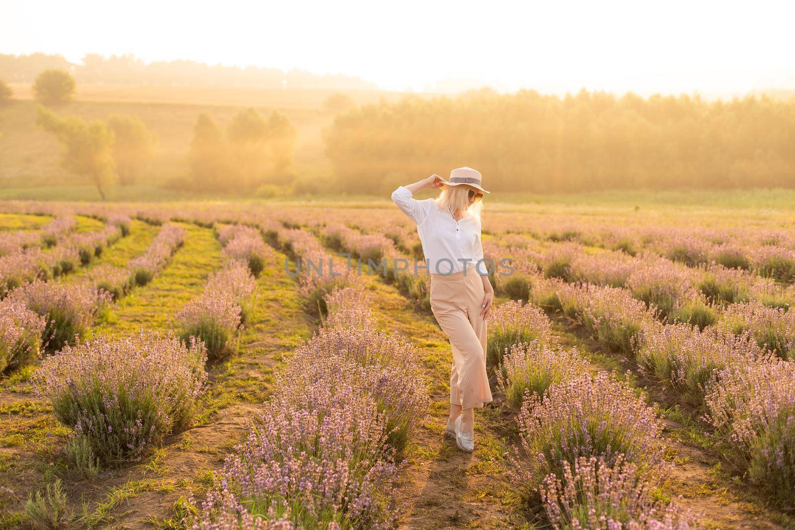 Young woman standing on a lavender field with sunrise on the background.