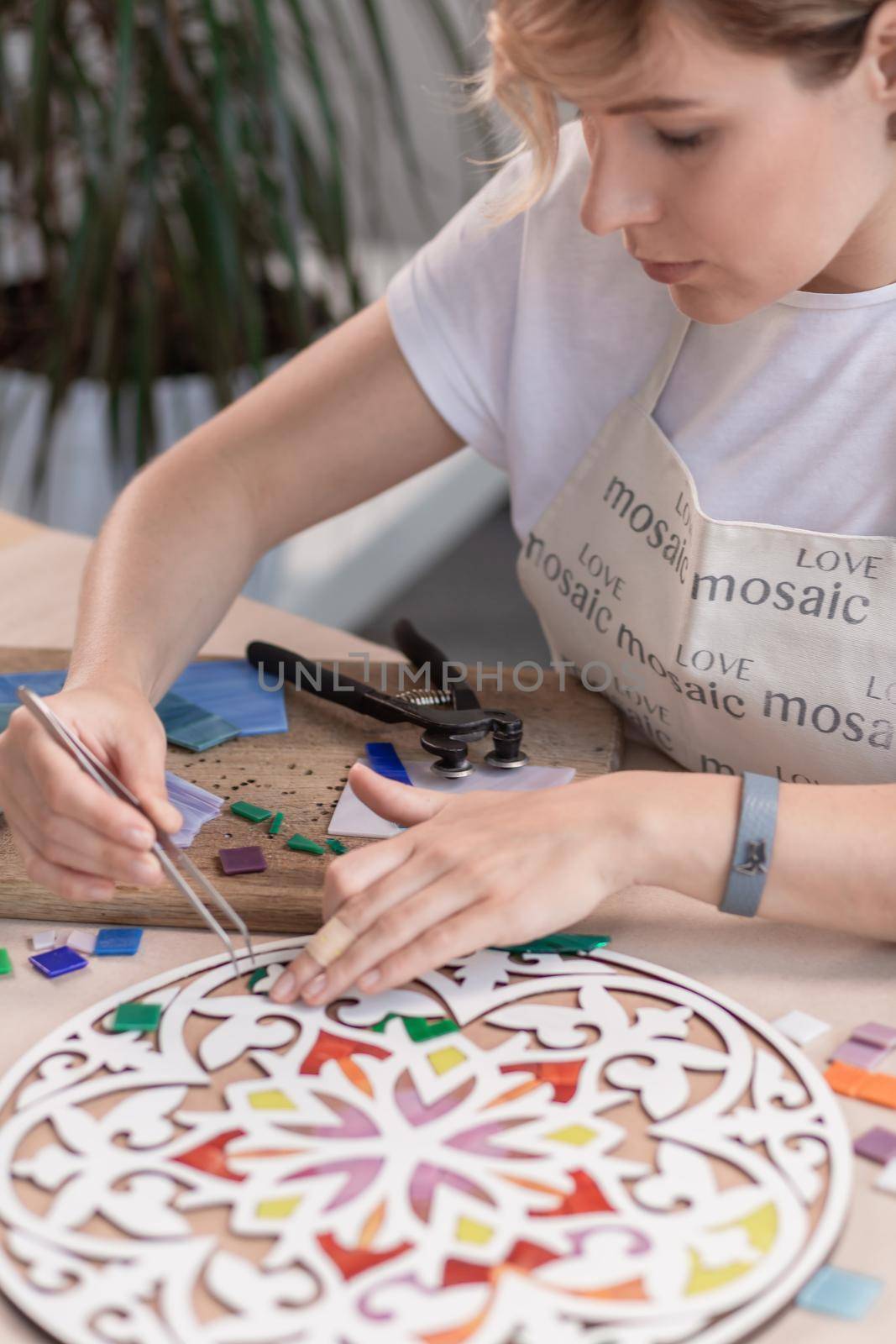 Workplace of the mosaic master: women's hands holding tool for mosaic details in the process of making a mosaic by nazarovsergey