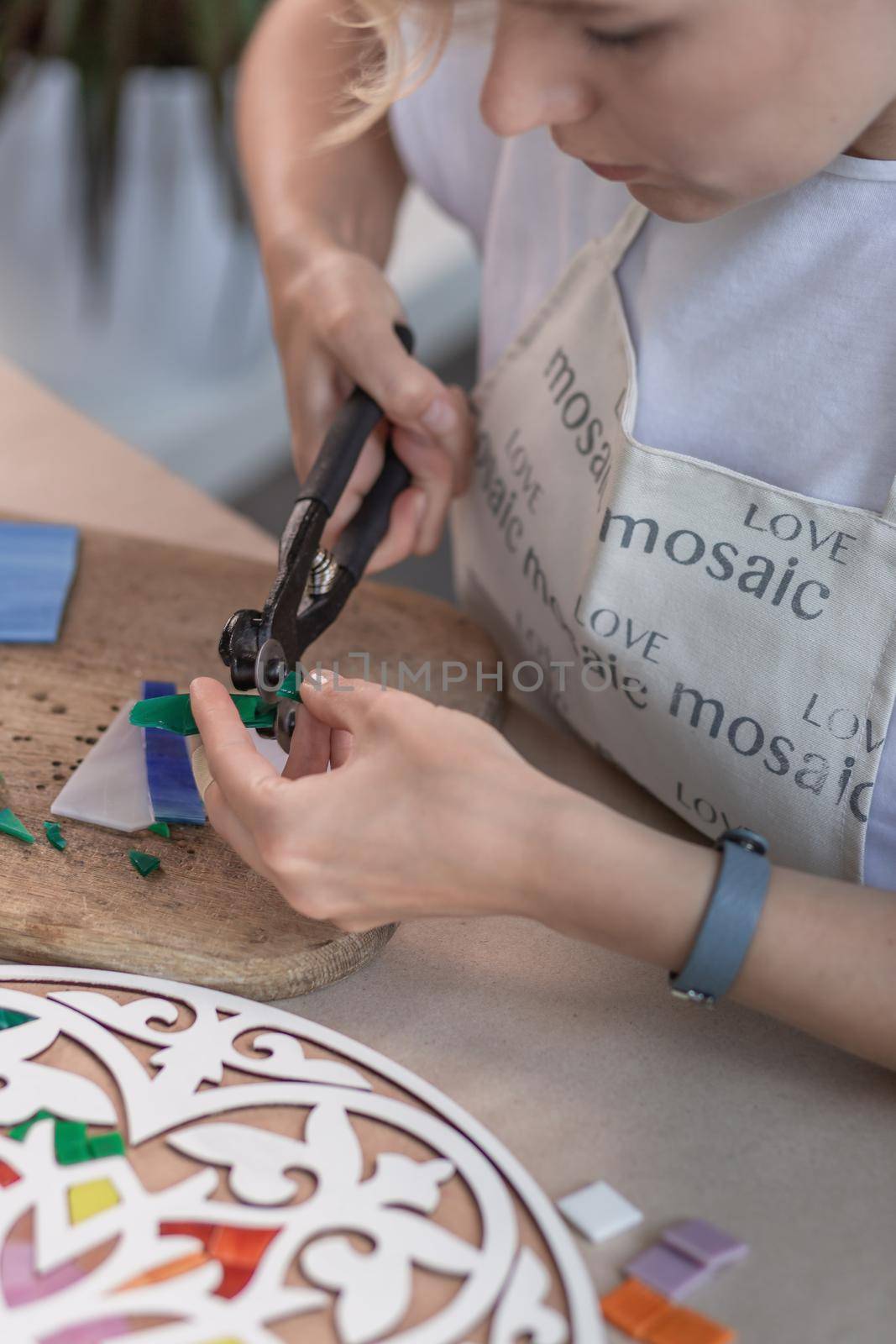 Workplace of the mosaic master: women's hands holding tool for mosaic details in the process of making a mosaic. Close-up. Creative process. Masterclass handmade