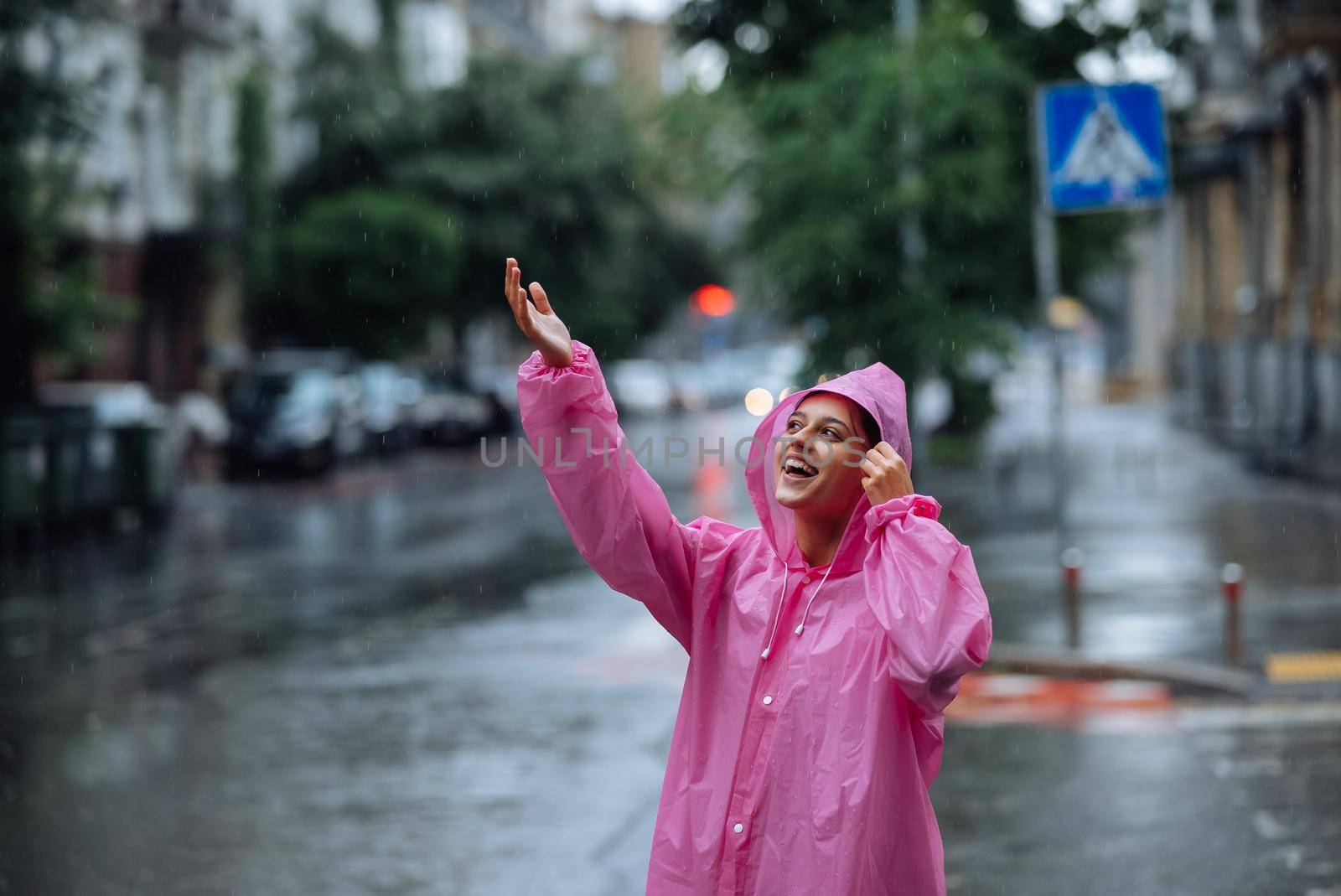 Young smiling woman with a pink raincoat on the street while enjoying a walk through the city on a rainy day.