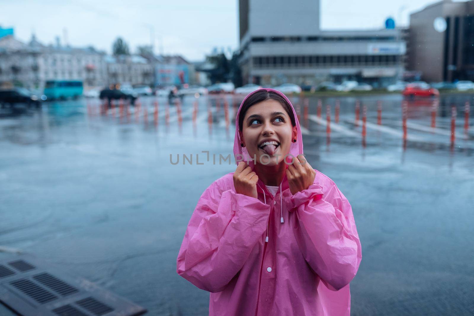 Young smiling woman with a pink raincoat on the street while enjoying a walk through the city on a rainy day.