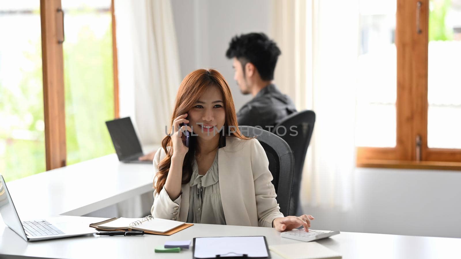 Attractive woman financial advisor having negotiations with client on mobile phone by prathanchorruangsak