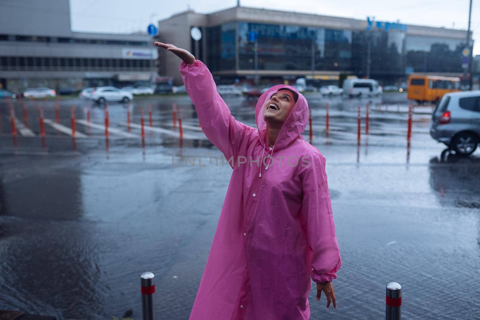 Young smiling woman with a pink raincoat on the street while enjoying a walk through the city on a rainy day.
