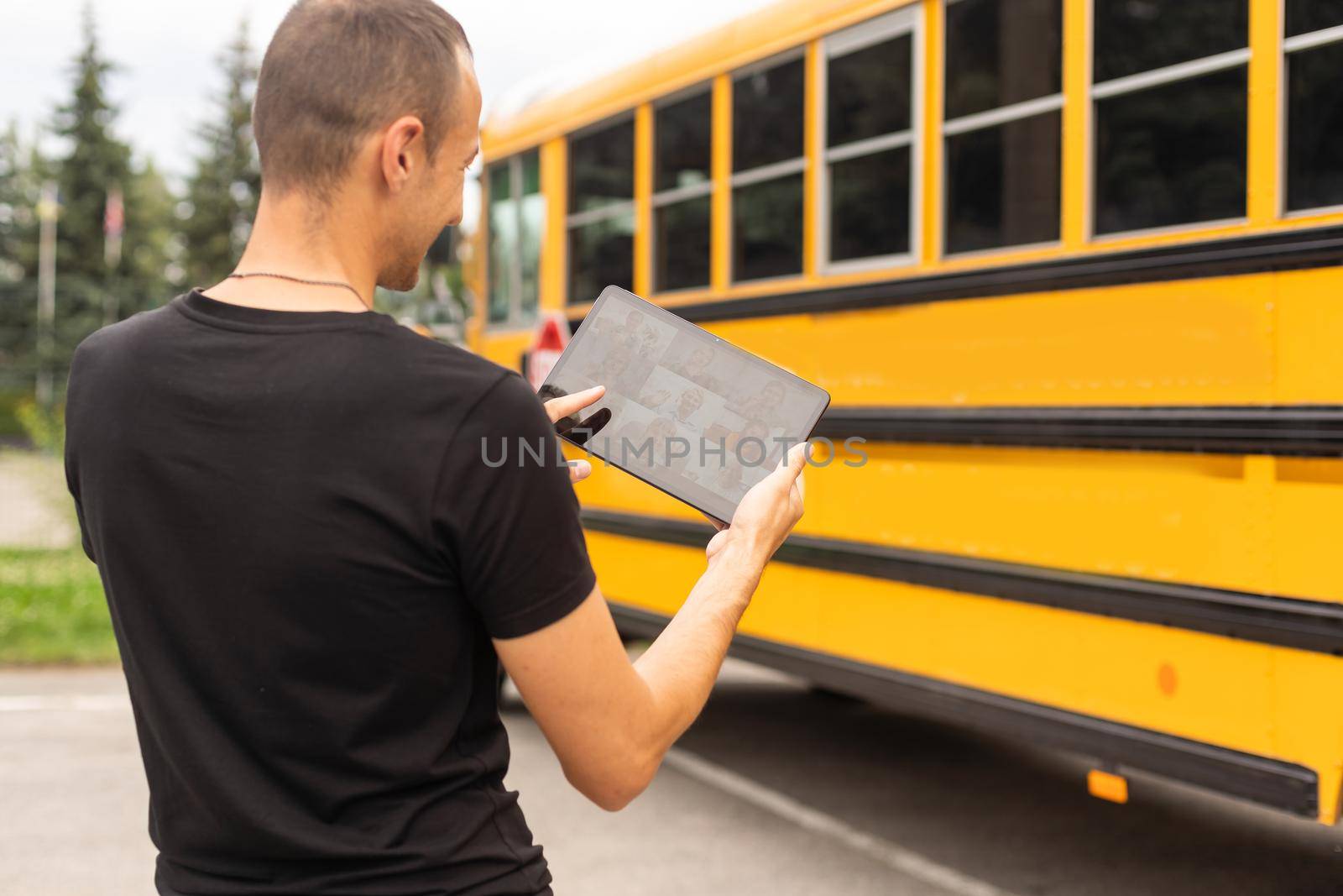 male Teacher Or Student With Digital Tablet near the school bus. video chat.