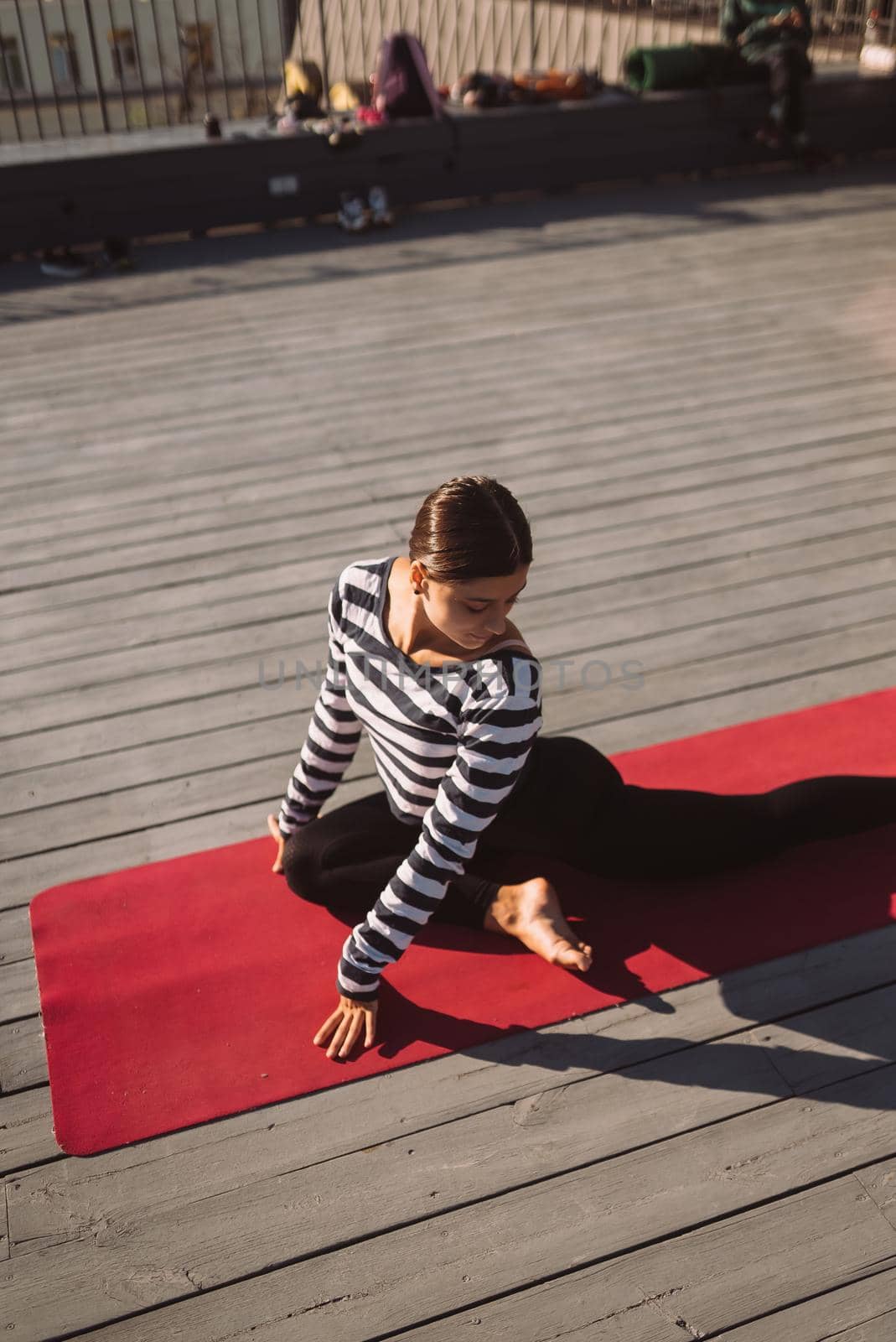 Young sporty happy woman in sportswear doing stretching exercises on yoga mat on house roof in early morning