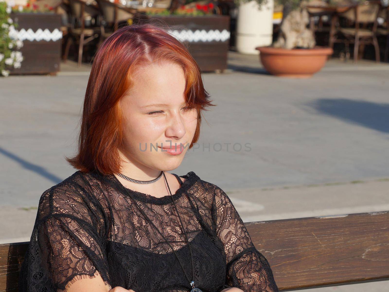 portrait of a teenage red-haired girl squinting from the sun.