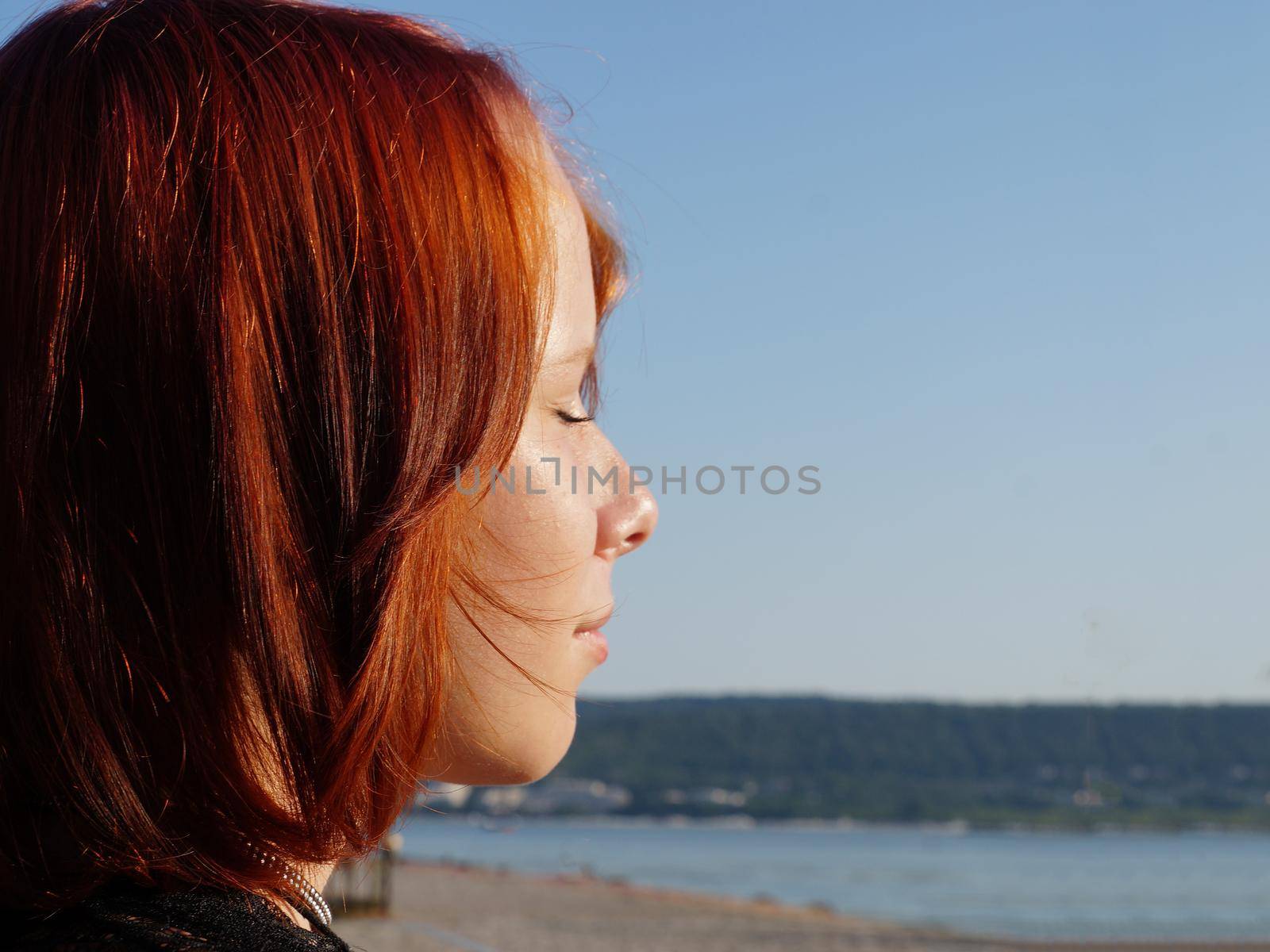 profile of a red-haired teenage girl with closed eyes close-up against the background of the sea, copy space.